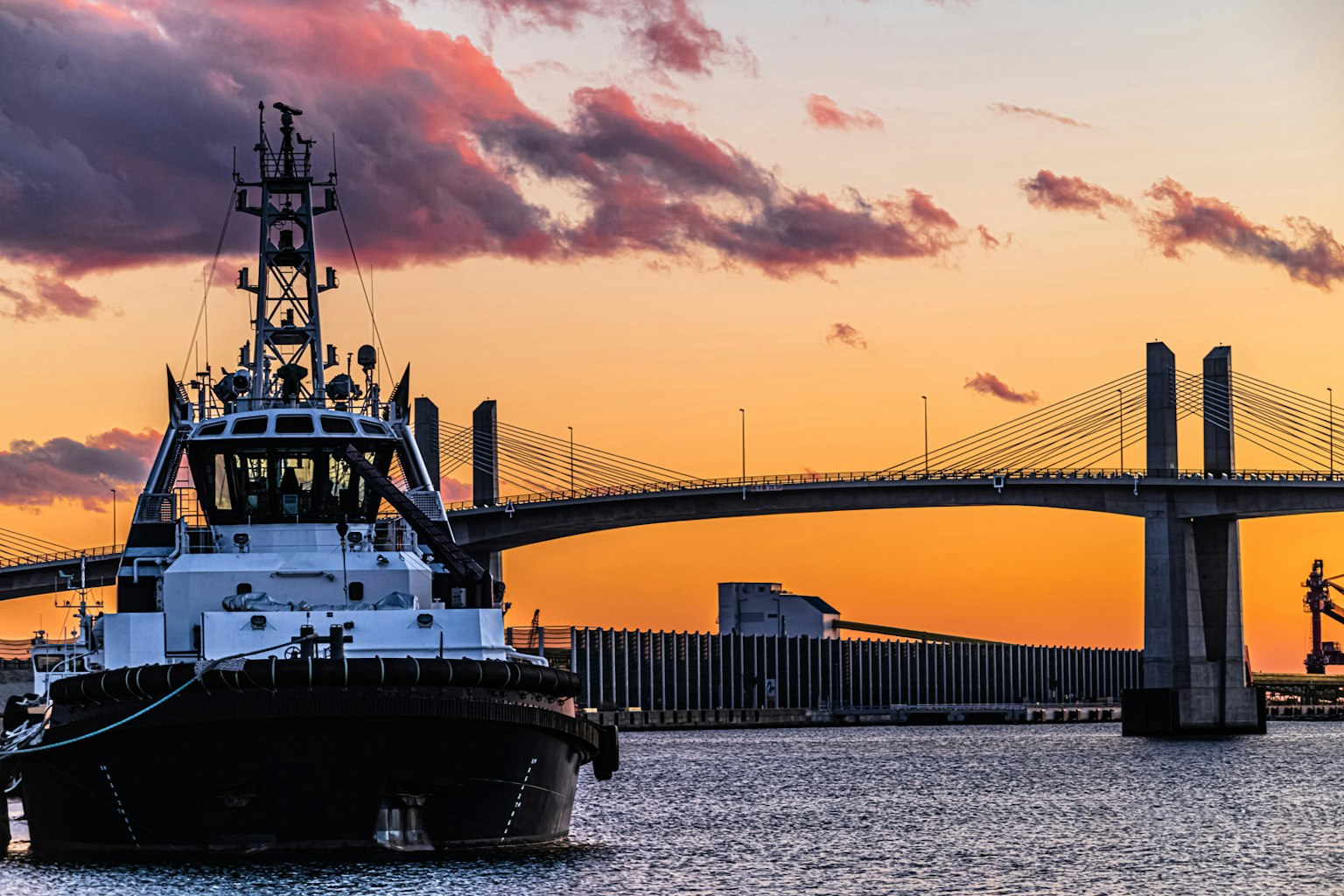 Tugboat in the foreground with a bridge and sunset sky