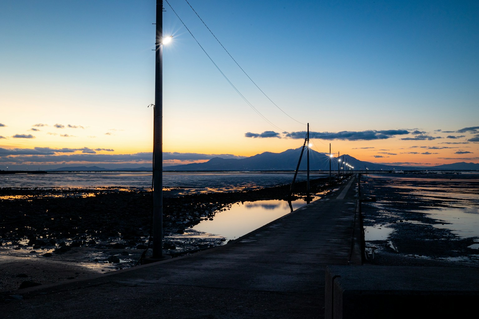 Chemin côtier s'étendant dans le coucher de soleil avec des montagnes en silhouette