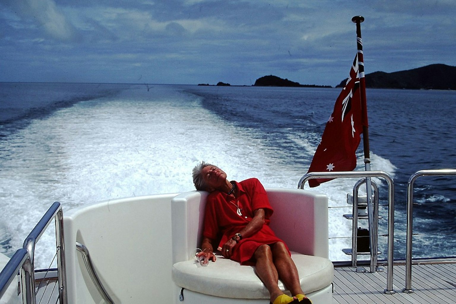 A woman in a red outfit reclining on a boat sofa with the ocean in the background