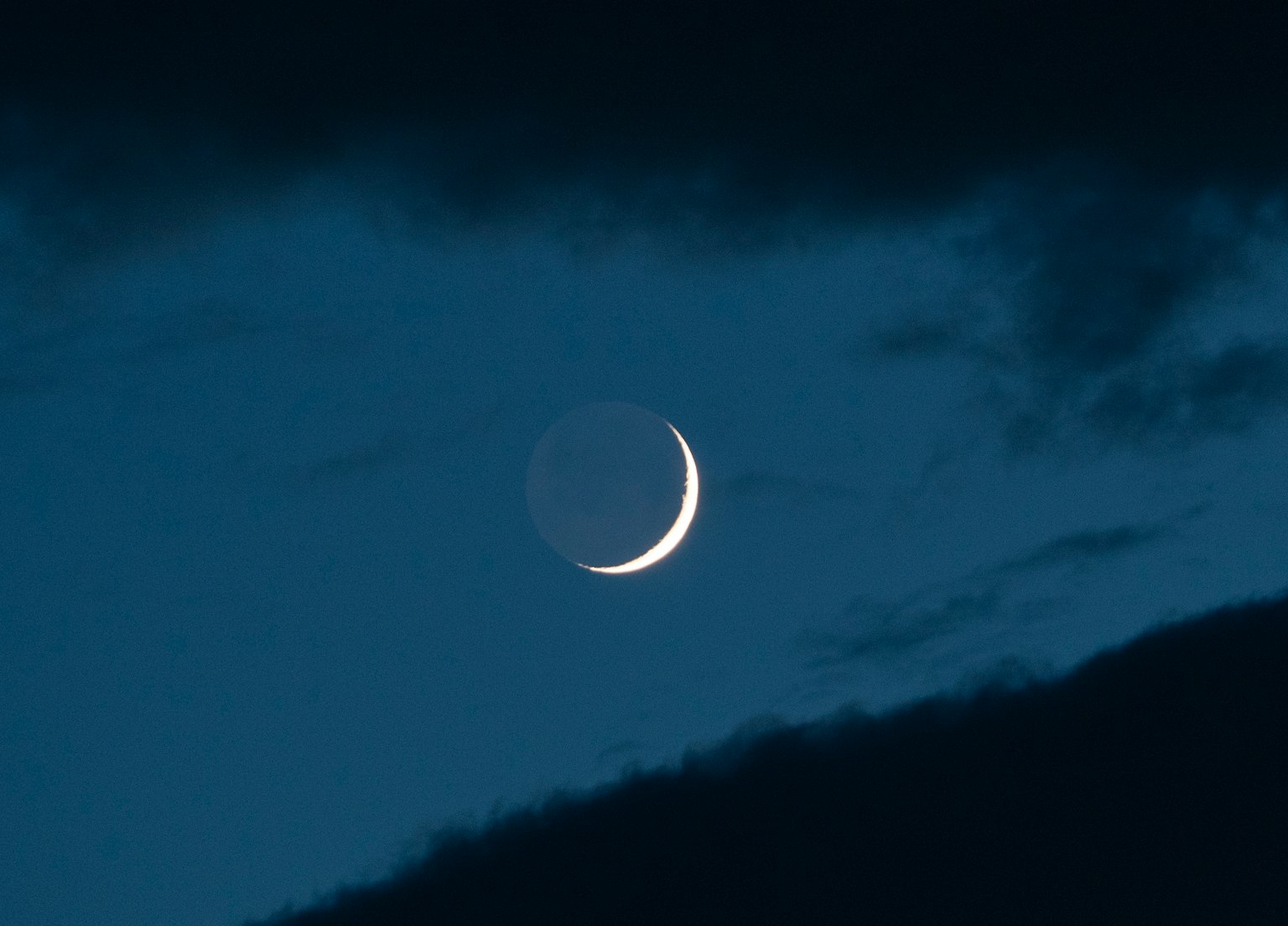 Luna crescente sottile in un cielo notturno blu con nuvole scure