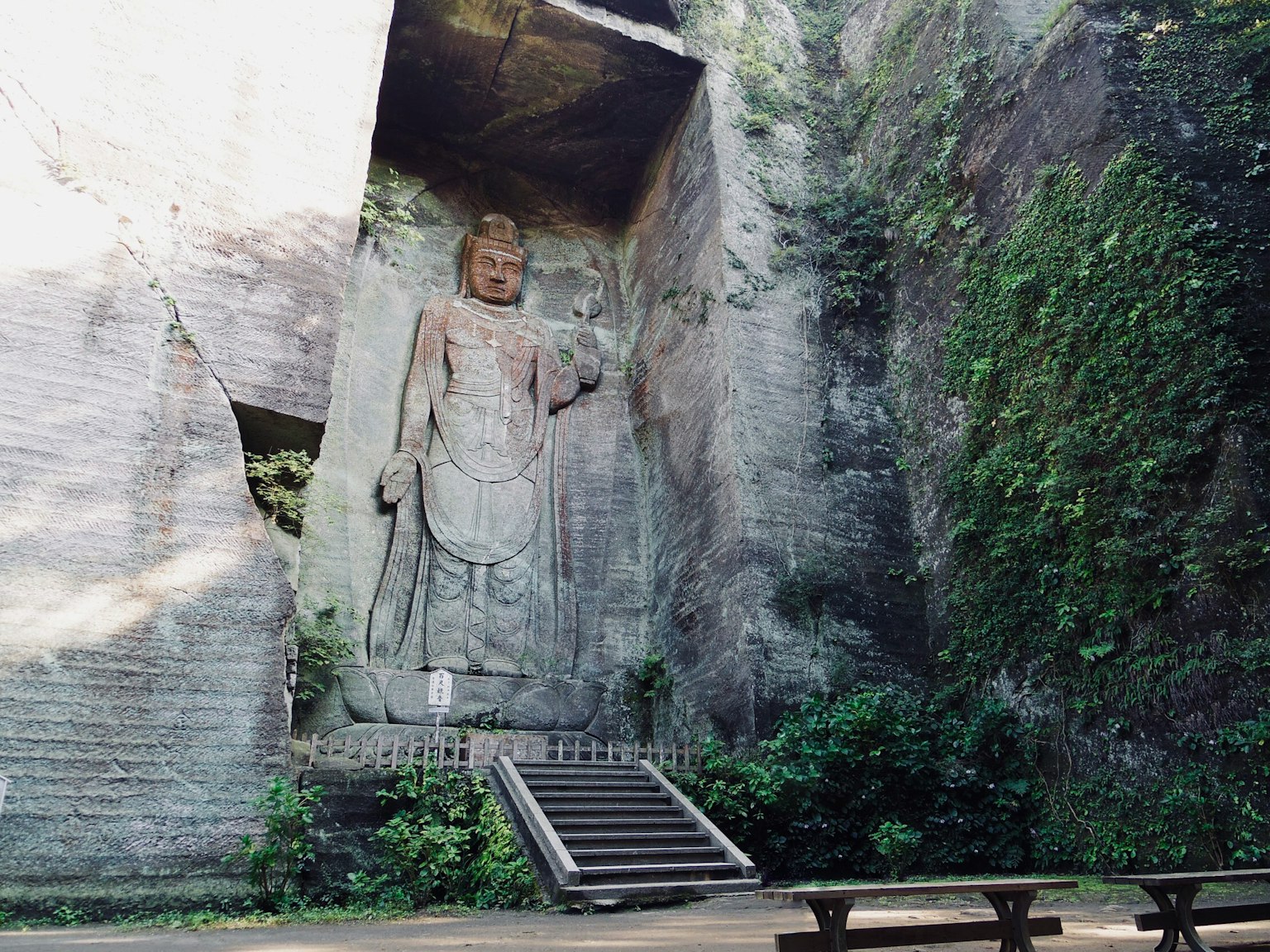 A large Buddha statue carved into a rock surrounded by greenery