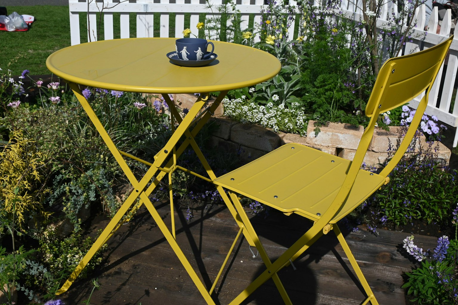 Ein kleiner gelber Tisch und Stuhl umgeben von Blumen in einem Garten