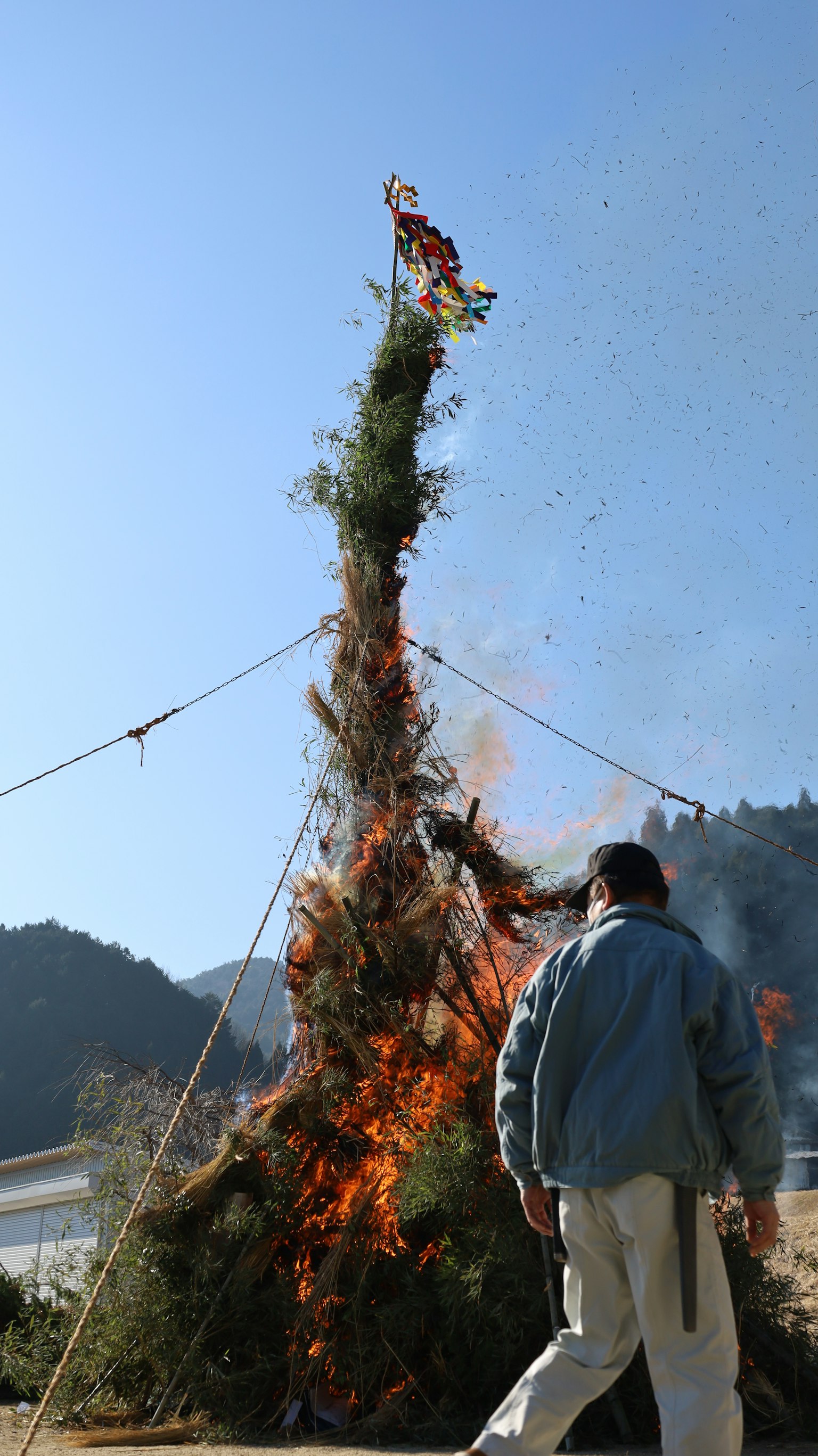 Ein Mann steht neben einem großen Lagerfeuer mit hohen Flammen