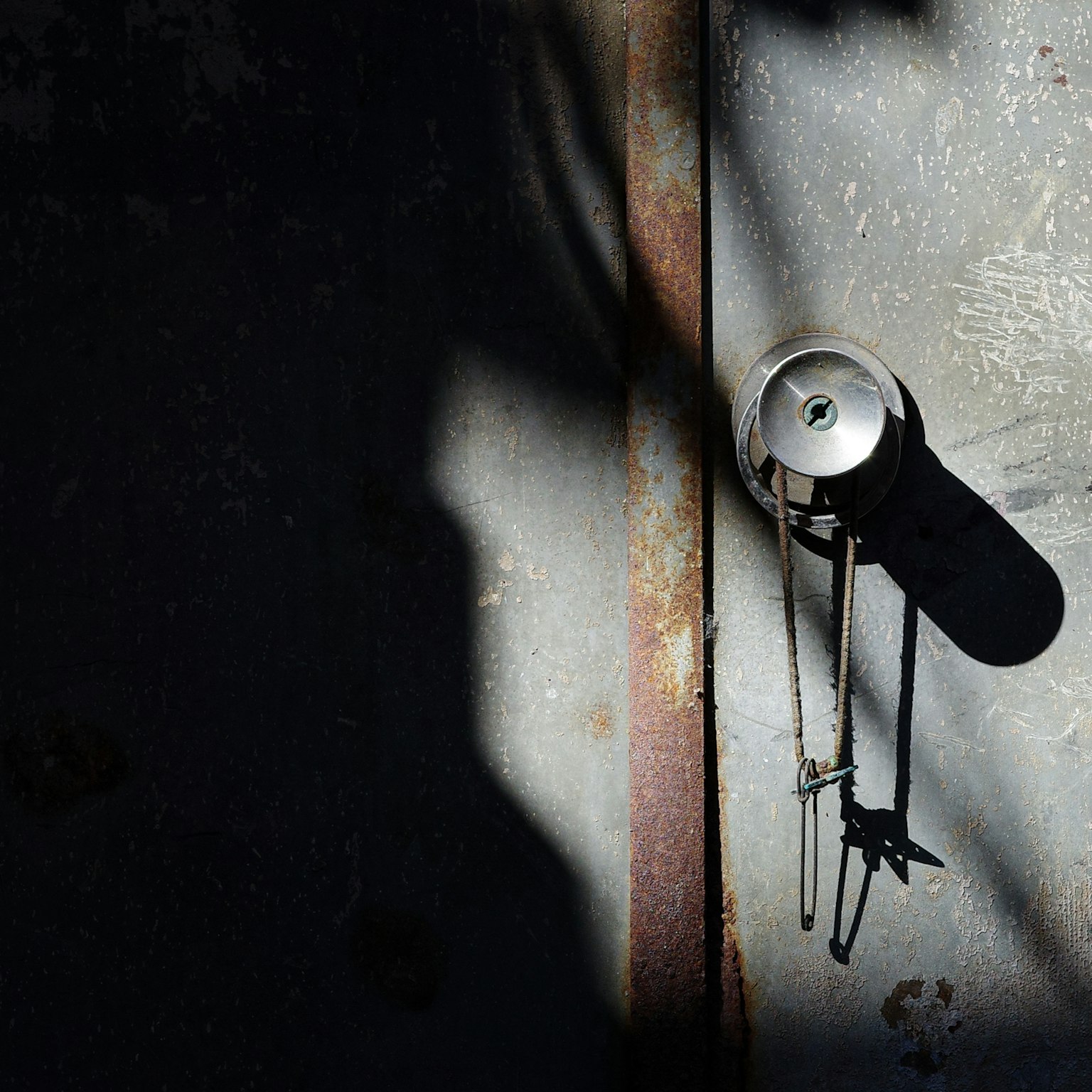 Puerta de metal antiguo con una campana colgante y sombra contrastante