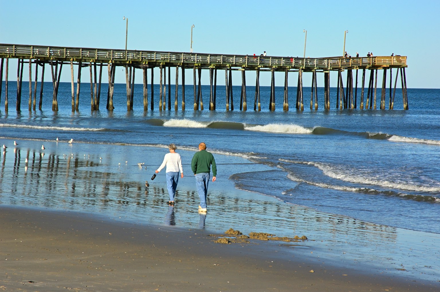 Paar, das am Strand mit einem Pier im Hintergrund spaziert