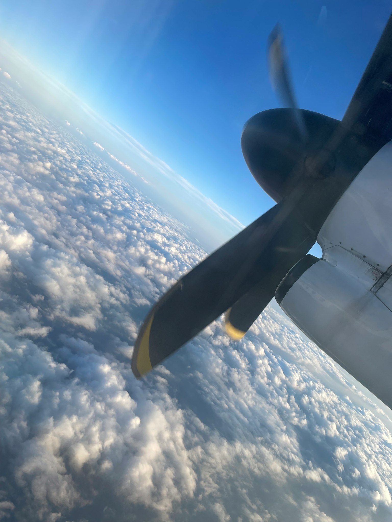 雲の上を飛ぶプロペラ機の翼と青い空