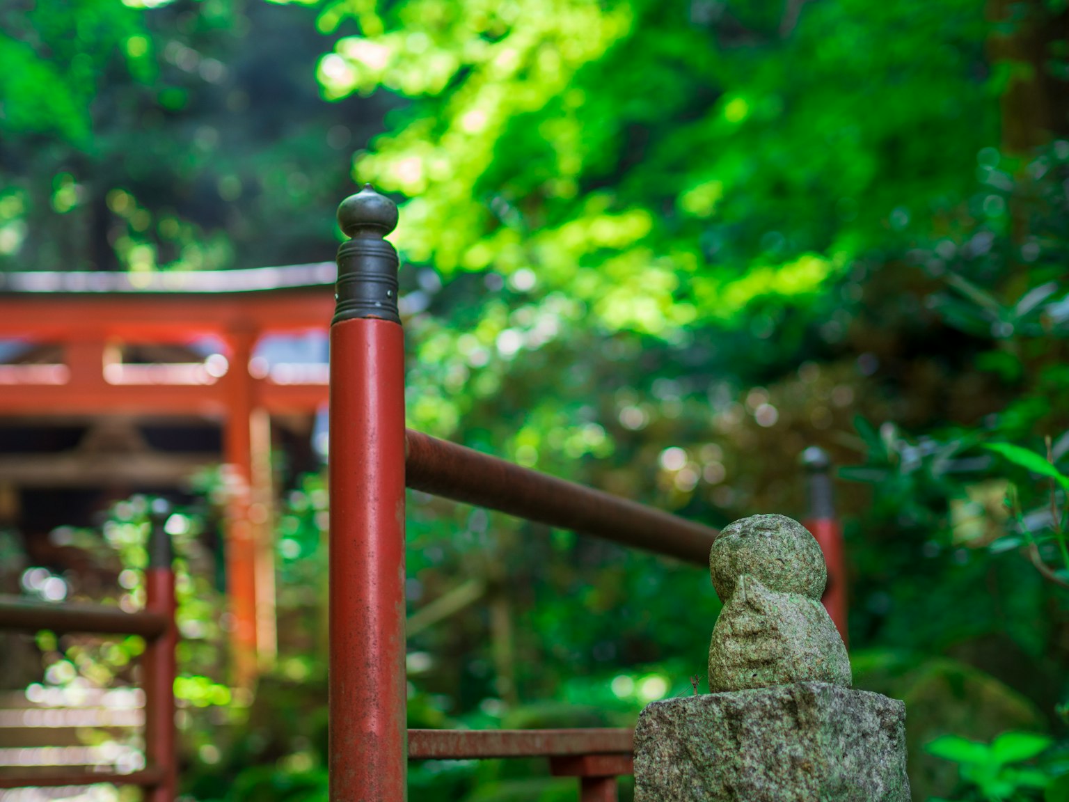 Una scena serena di un ponte rosso e una statua di pietra in una foresta verdeggiante