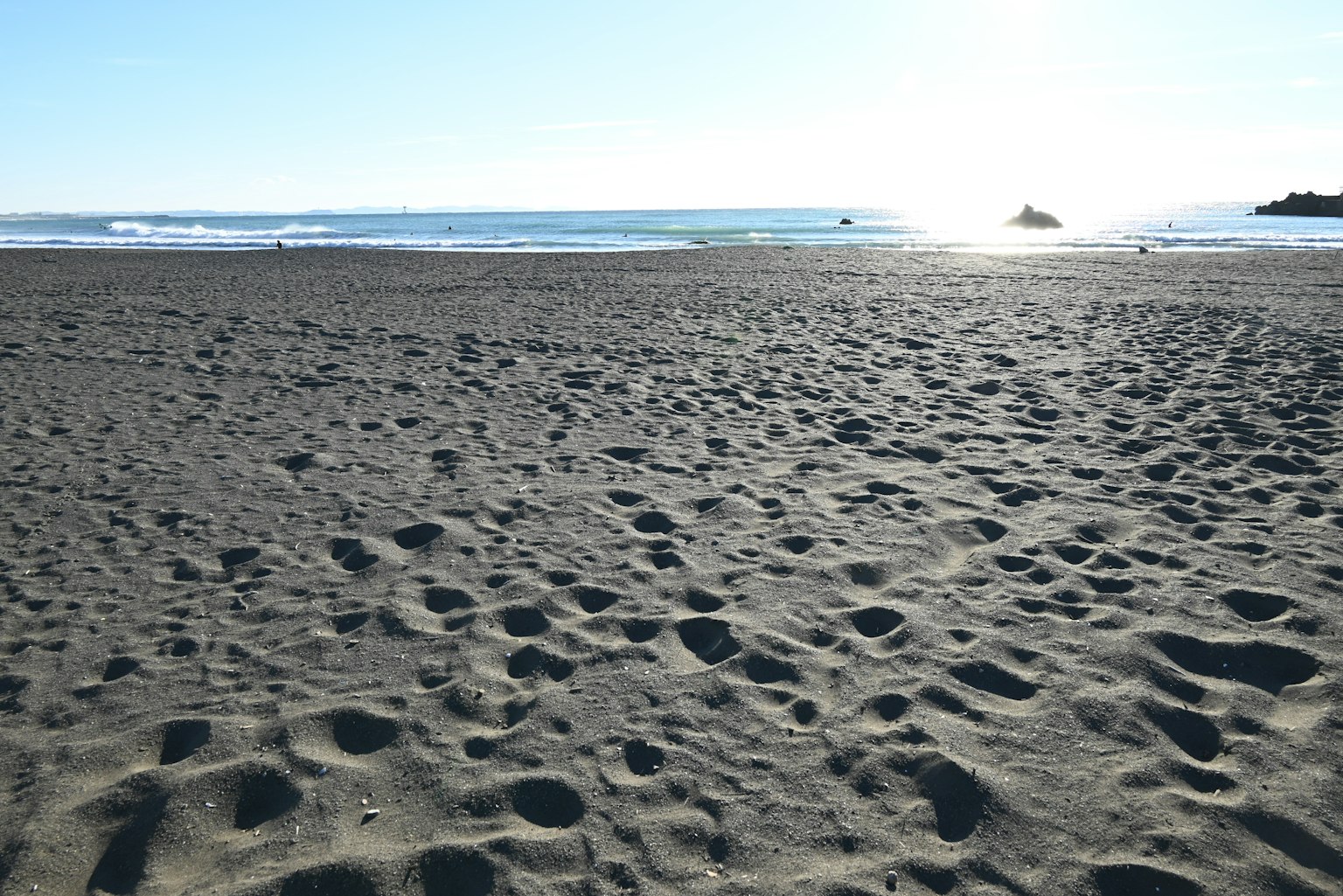 Ein Sandstrand mit verstreuten Fußabdrücken und einem blauen Meer und Himmel