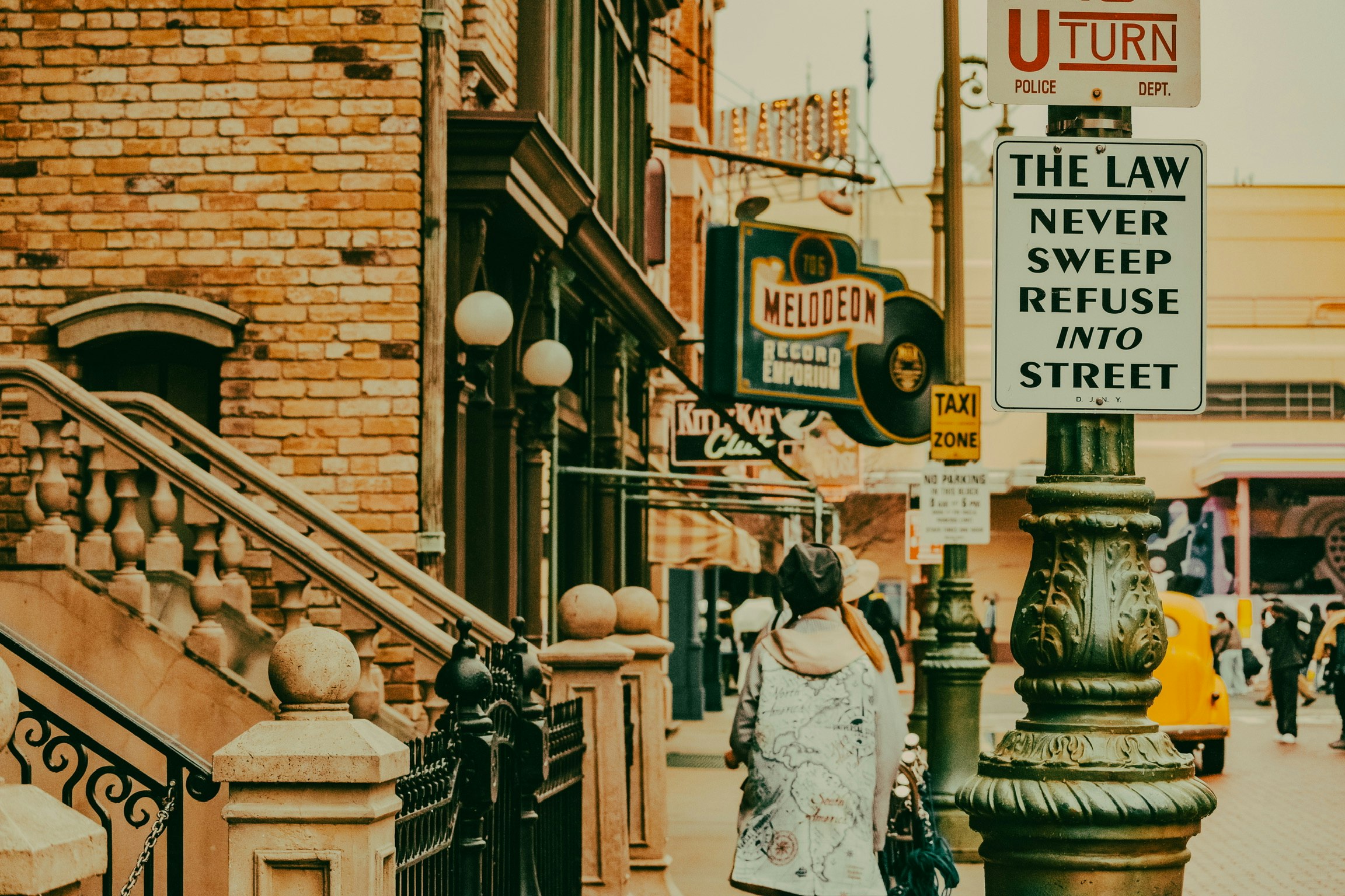 street scene with brick alley, signs, and people walking near a staircase