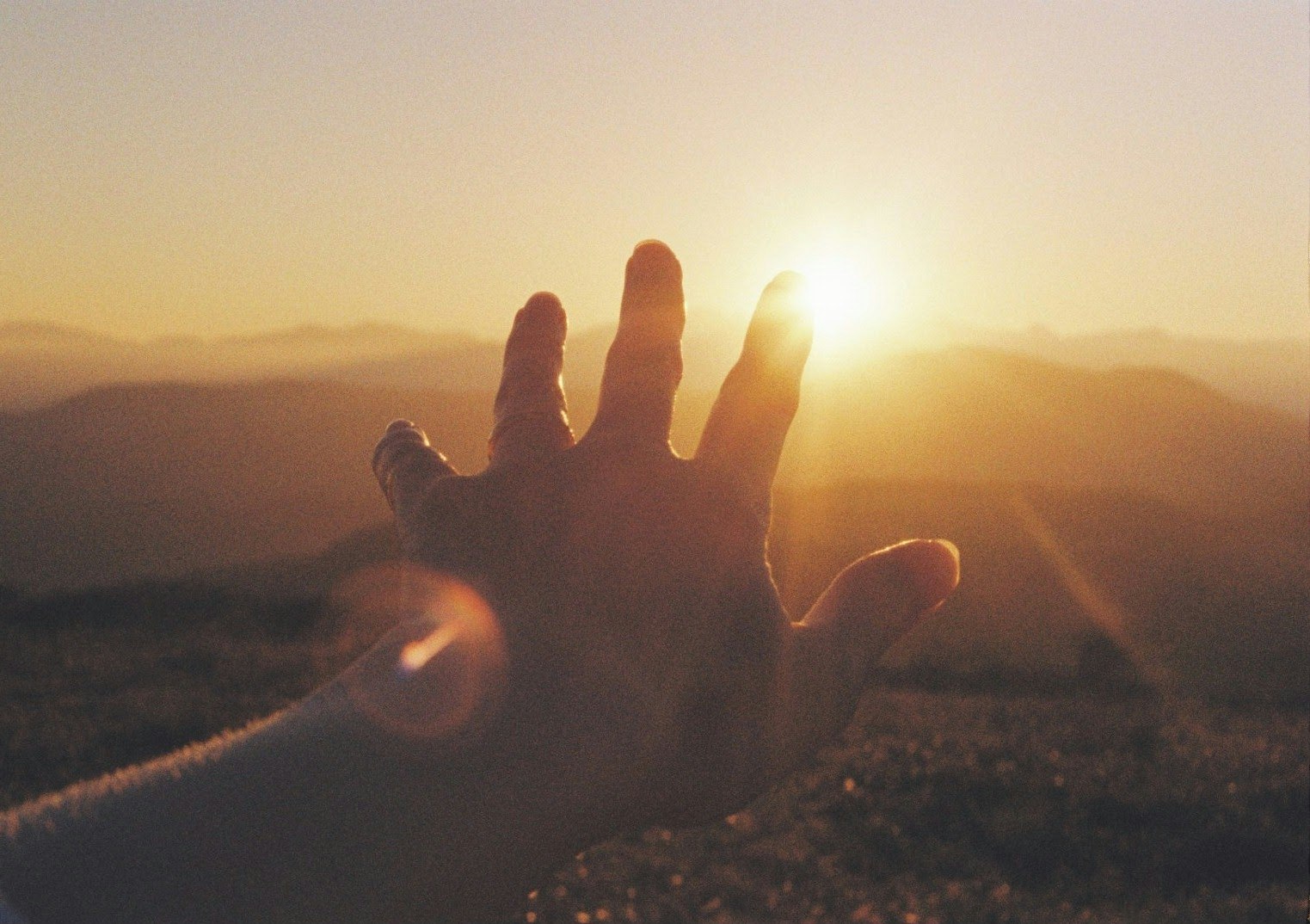 Hand in Silhouette vor dem Sonnenuntergang über sanften Hügeln