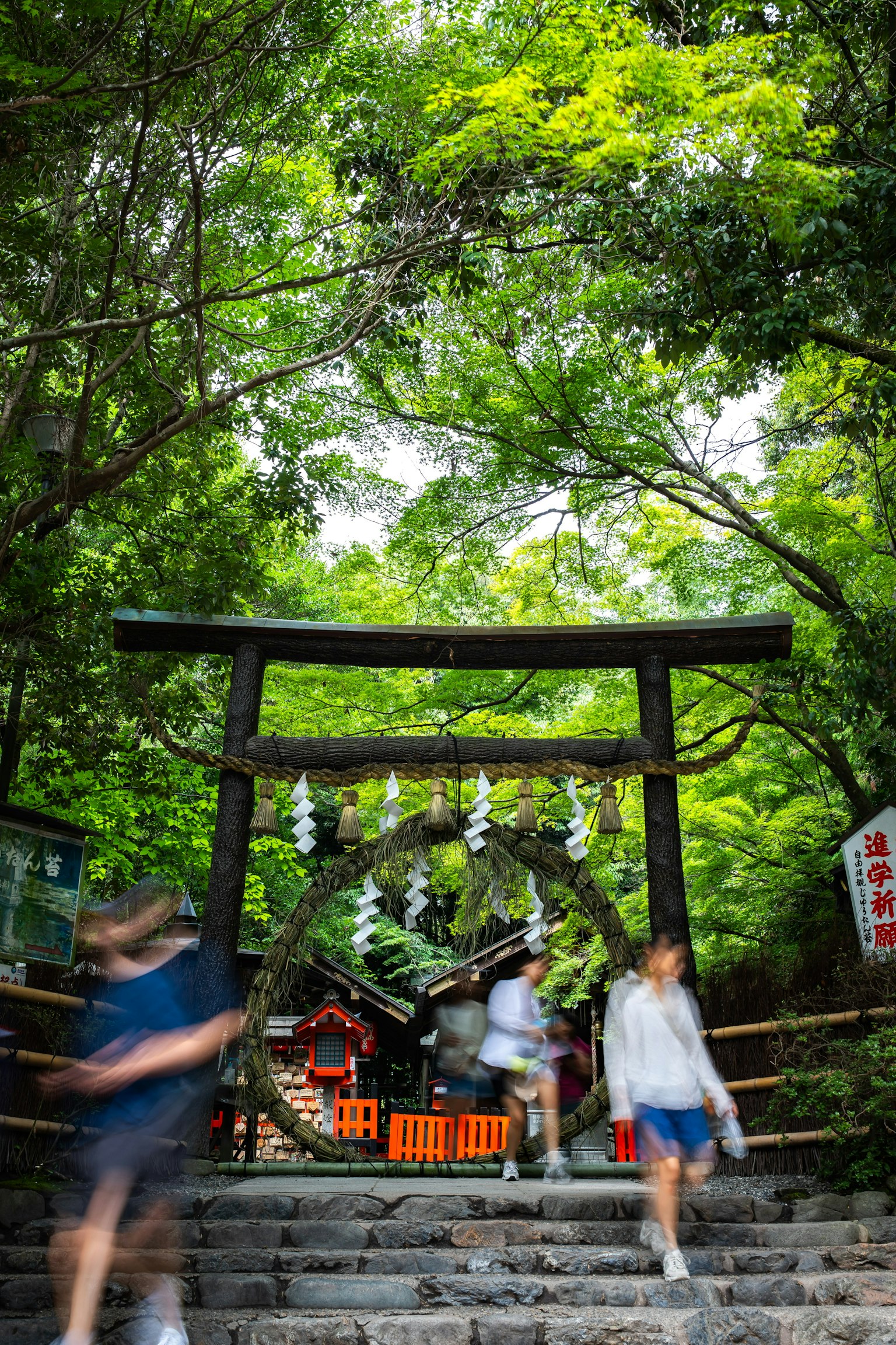 Un torii circondato da una vegetazione lussureggiante con persone che passano