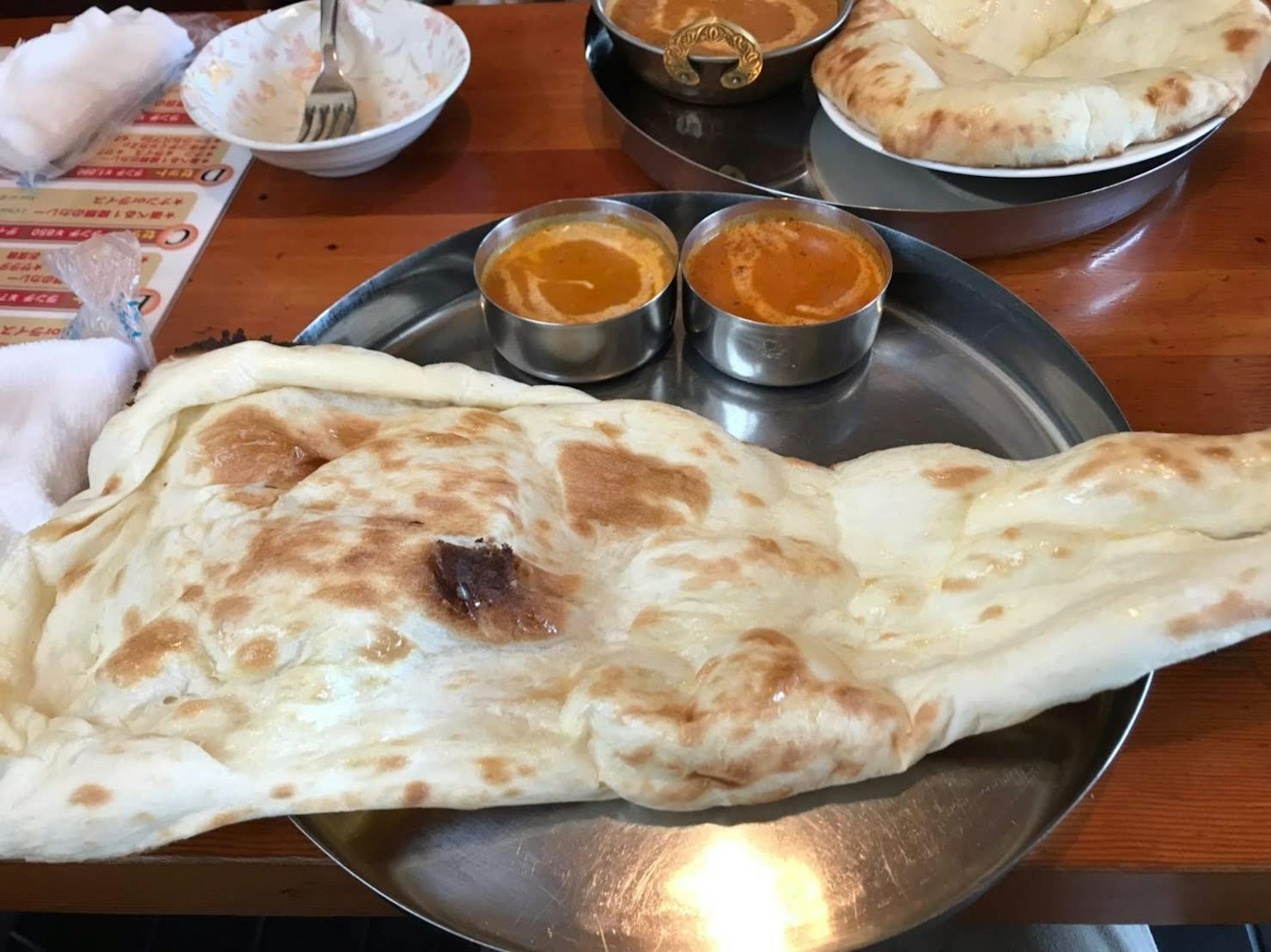 Large naan bread with two bowls of curry on a metal plate