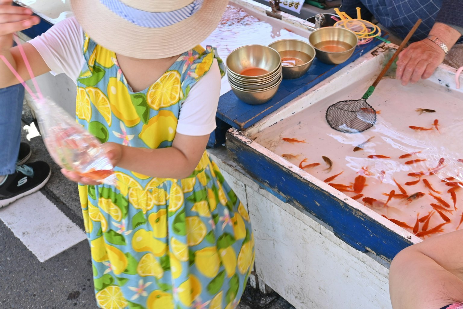 A girl wearing a lemon-patterned dress enjoying goldfish scooping
