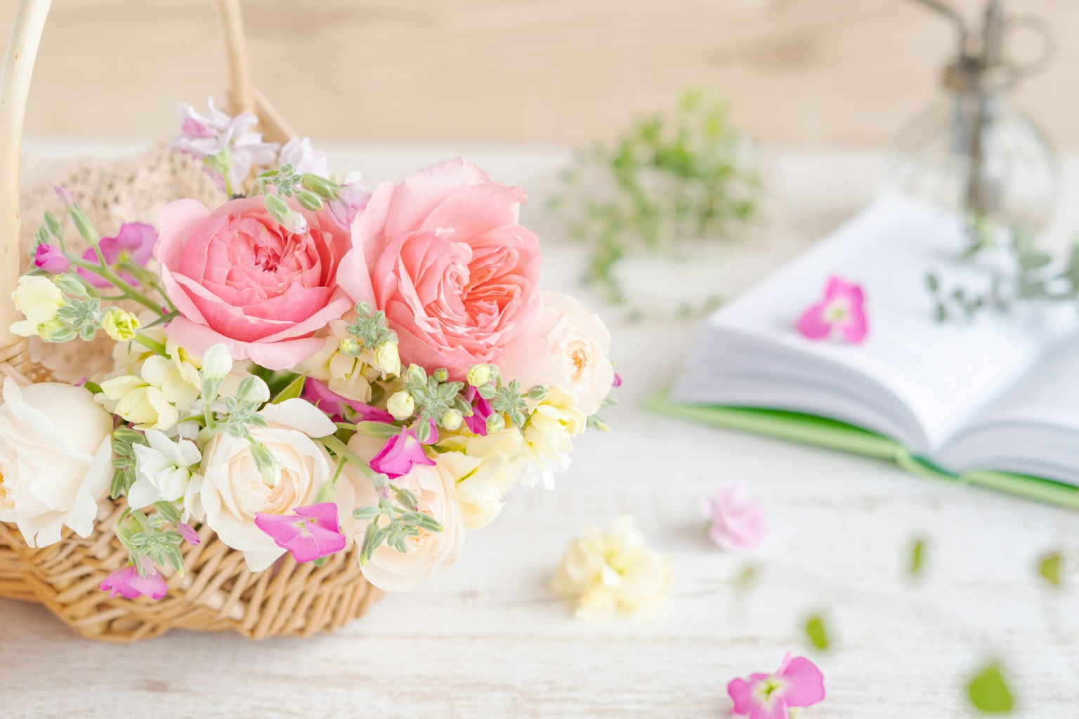 Un cesto pieno di rose rosa e fiori bianchi accanto a un libro aperto con piccoli fiori sparsi