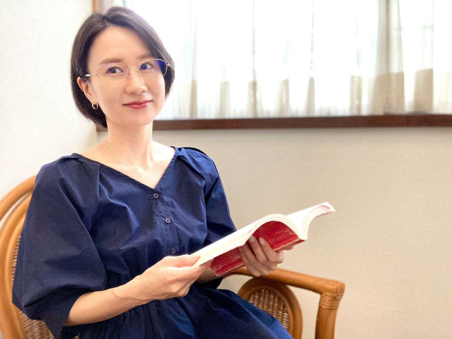Chân dung của một người phụ nữ ngồi trên ghế đọc sách với ánh sáng tự nhiên từ cửa sổ