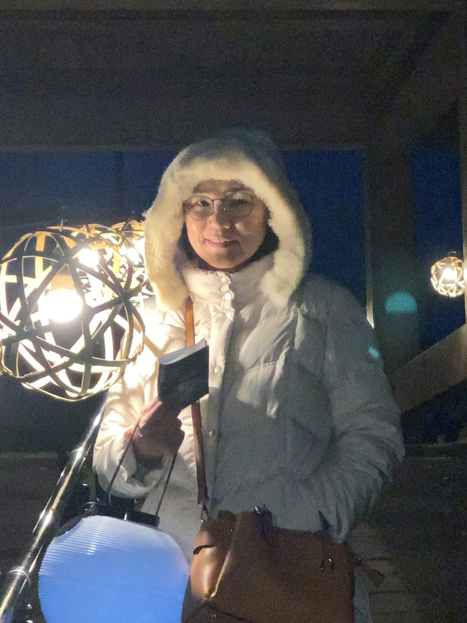 Una donna in piedi in una giacca a vento bianca di notte Luci decorative brillano sullo sfondo