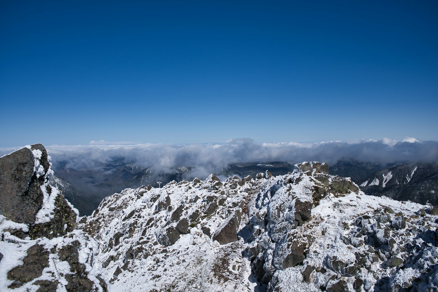View from a snowy mountain peak with clear blue sky and distant clouds