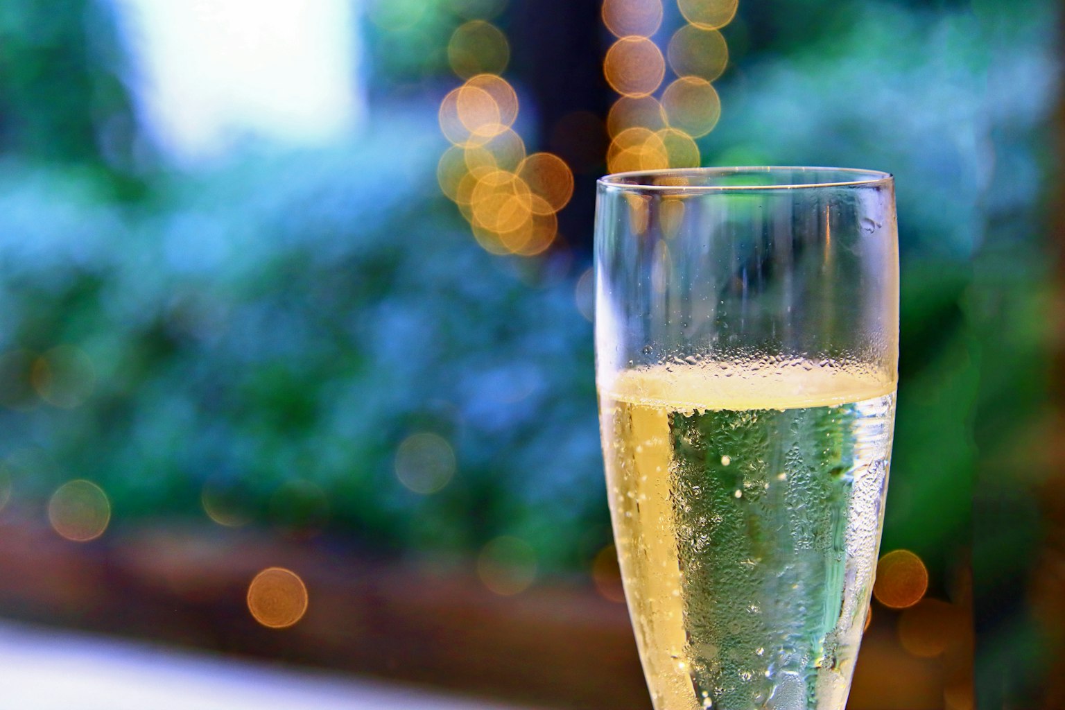 Close-up of a champagne glass filled with bubbles blurred green background with bright lights