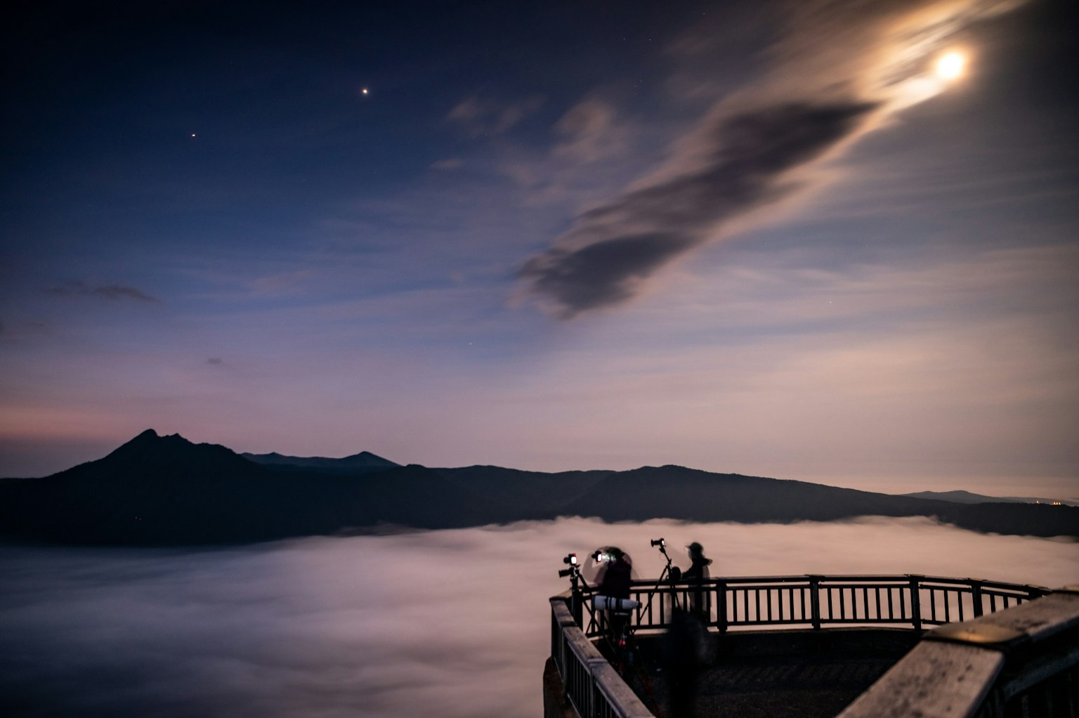 Pemandangan pegunungan dengan bulan dan bintang di langit malam di atas lautan awan