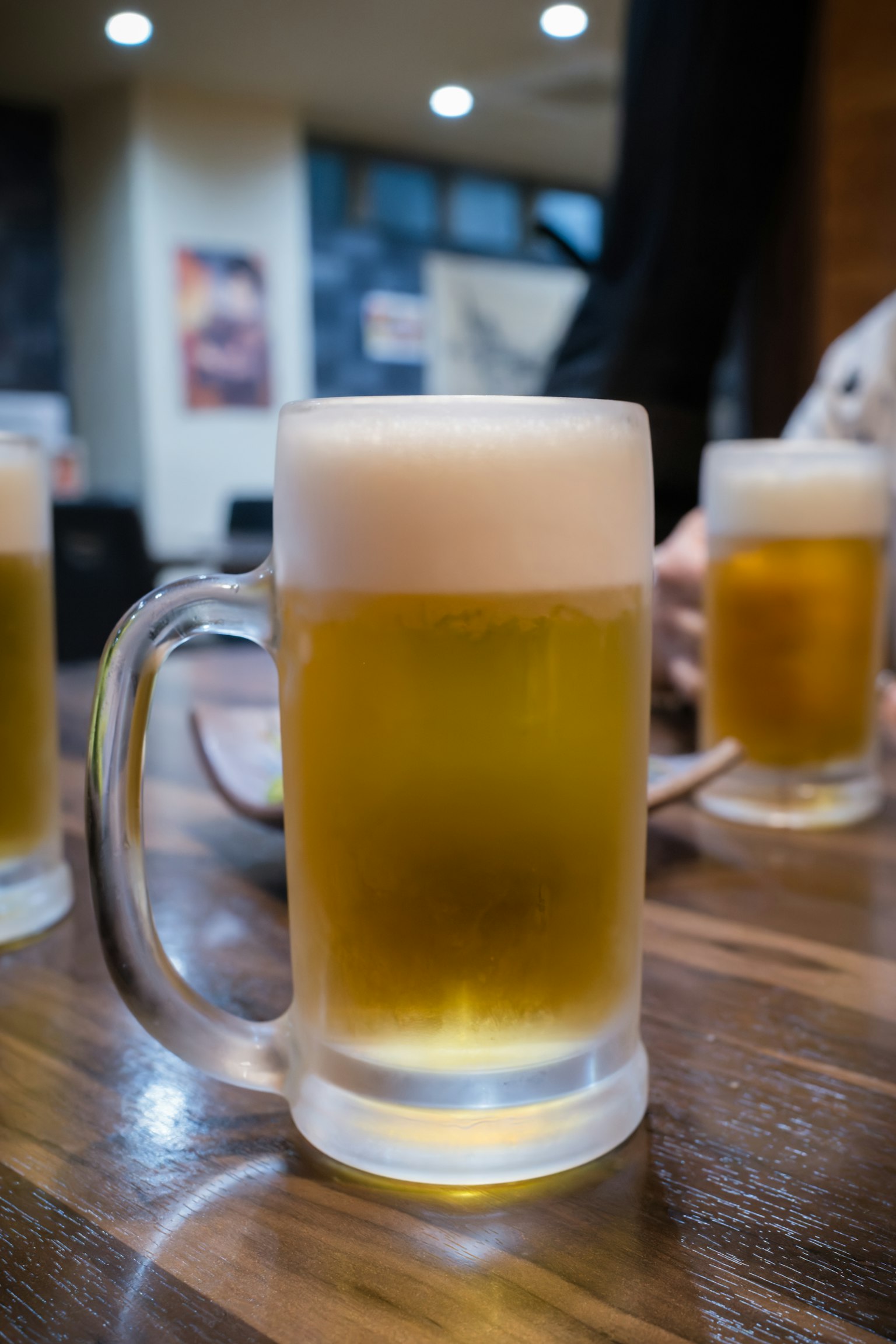 A frothy beer in a clear mug placed on a wooden table