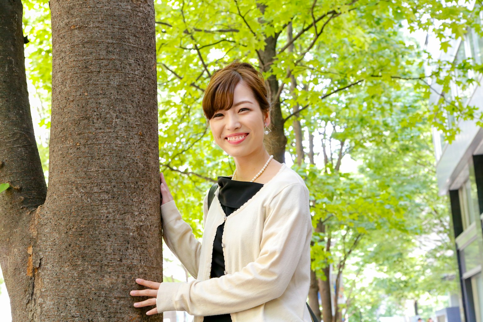 Smiling woman leaning against a tree among green foliage