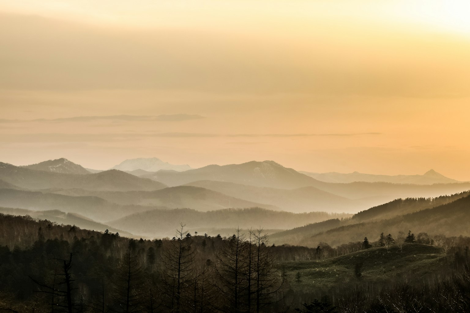 Paisaje de montañas al atardecer cielo naranja suave y colinas brumosas