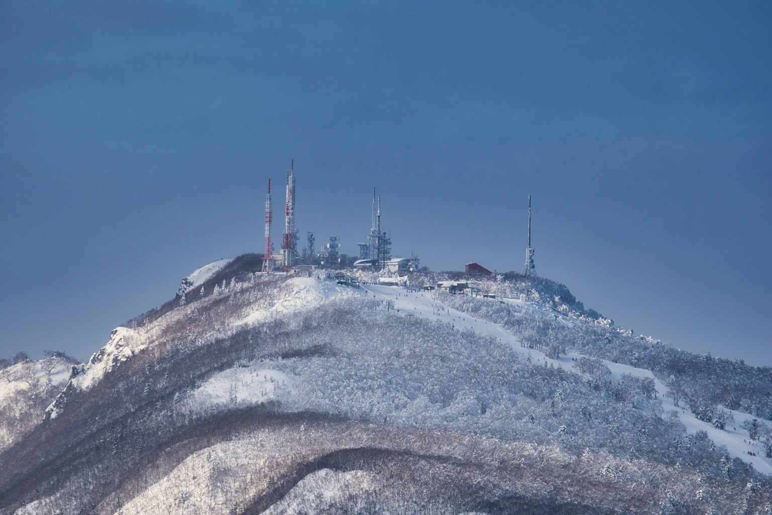 Snow-covered mountain peak with communication towers and cold sky