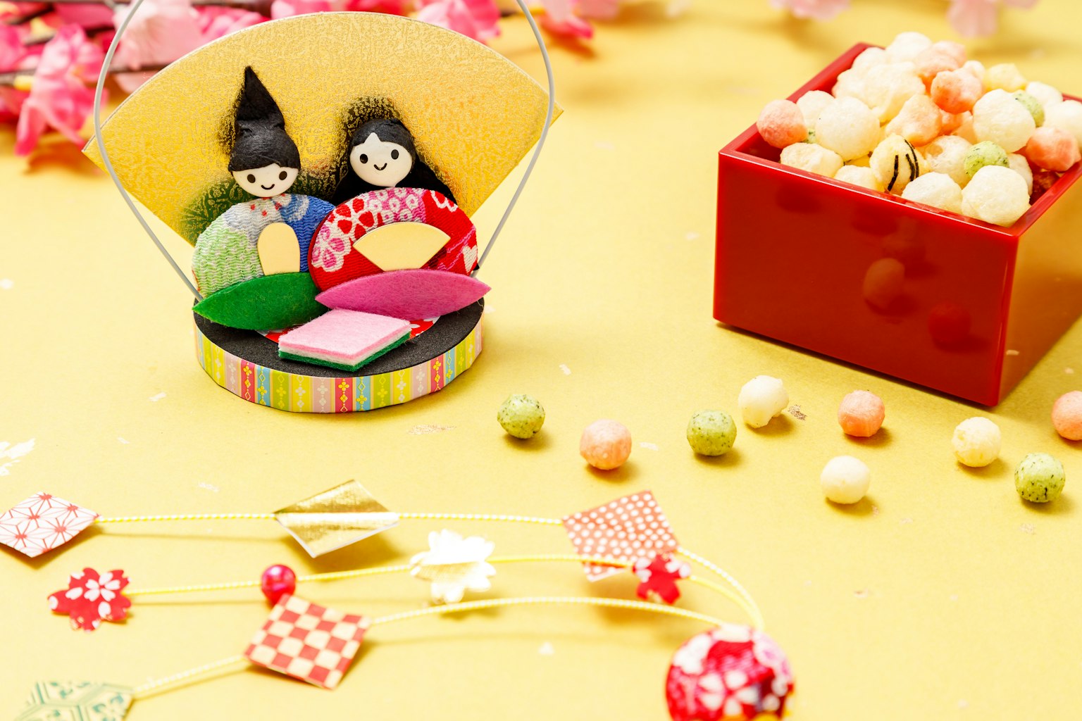 Dos muñecas sentadas sobre un fondo amarillo con cajas de caramelos coloridos
