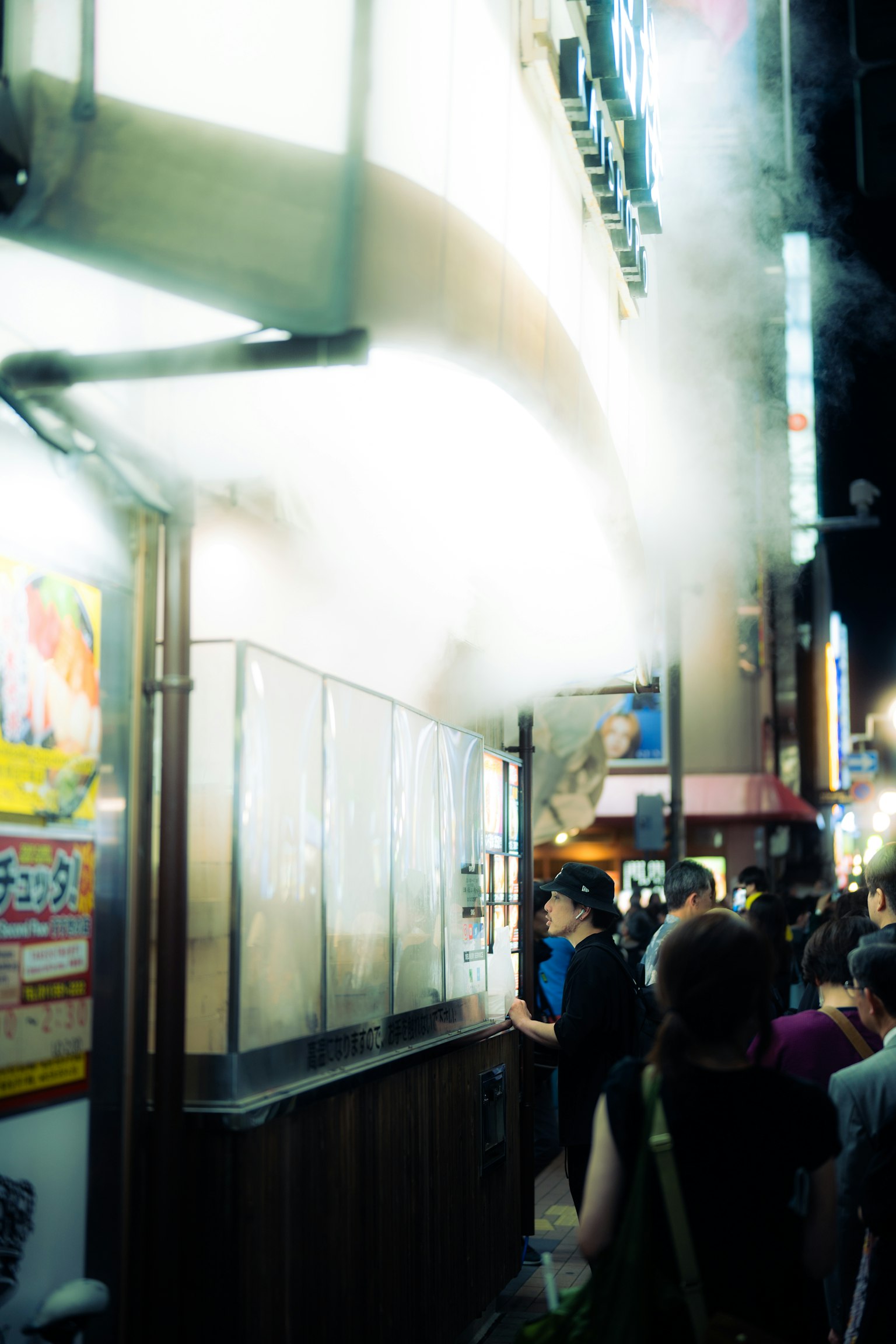 Puesto de comida callejera emitiendo vapor con gente en una escena nocturna bulliciosa