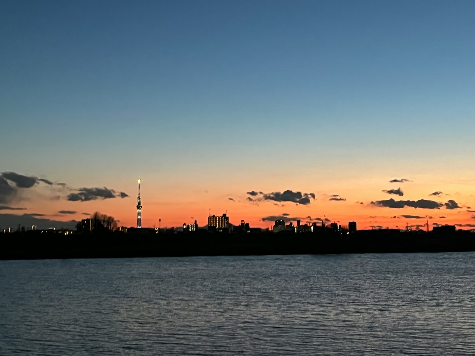 City silhouette reflecting in water under a sunset sky