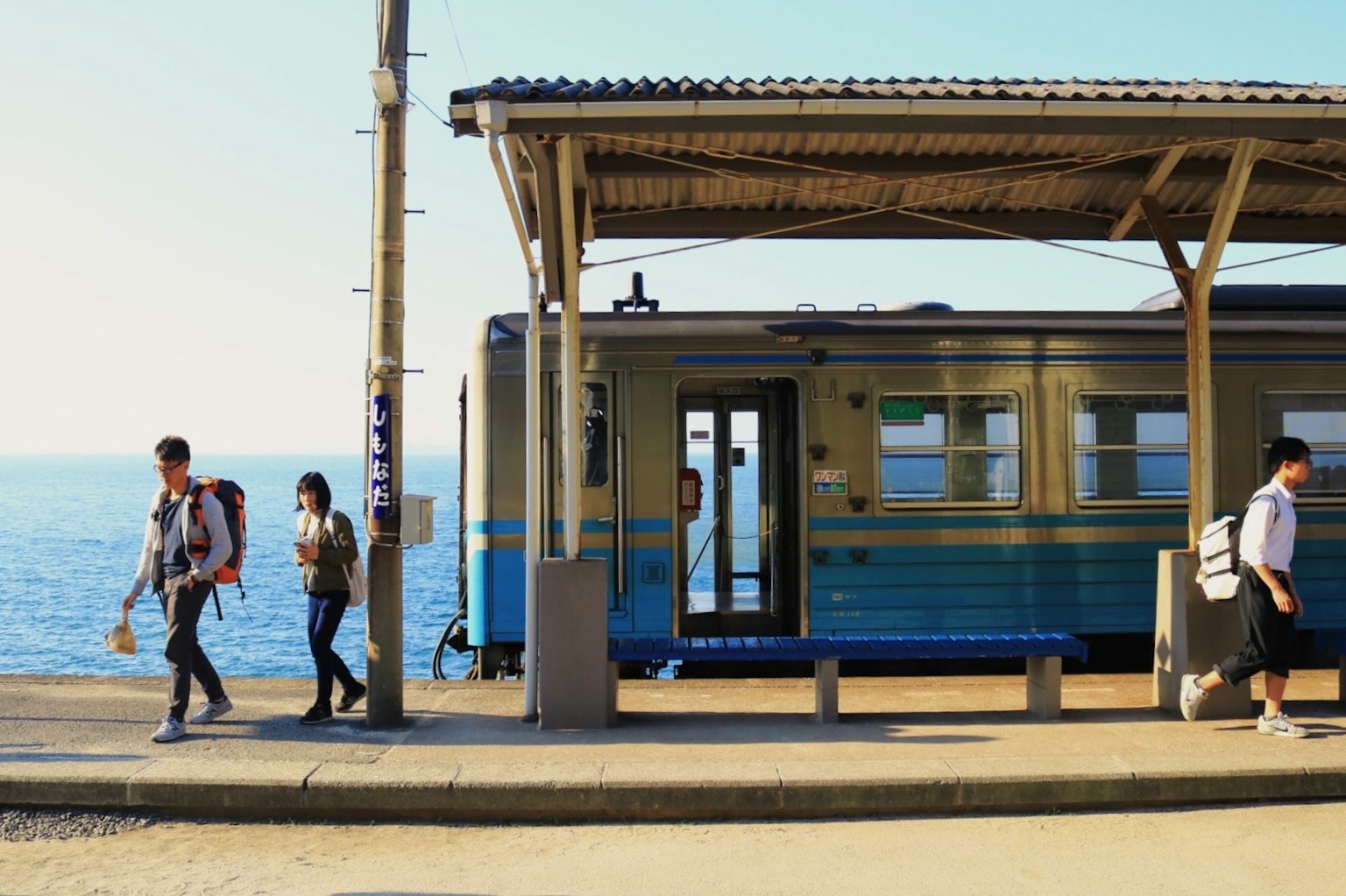 Passeggeri che camminano in una stazione ferroviaria vicino al mare con un treno blu