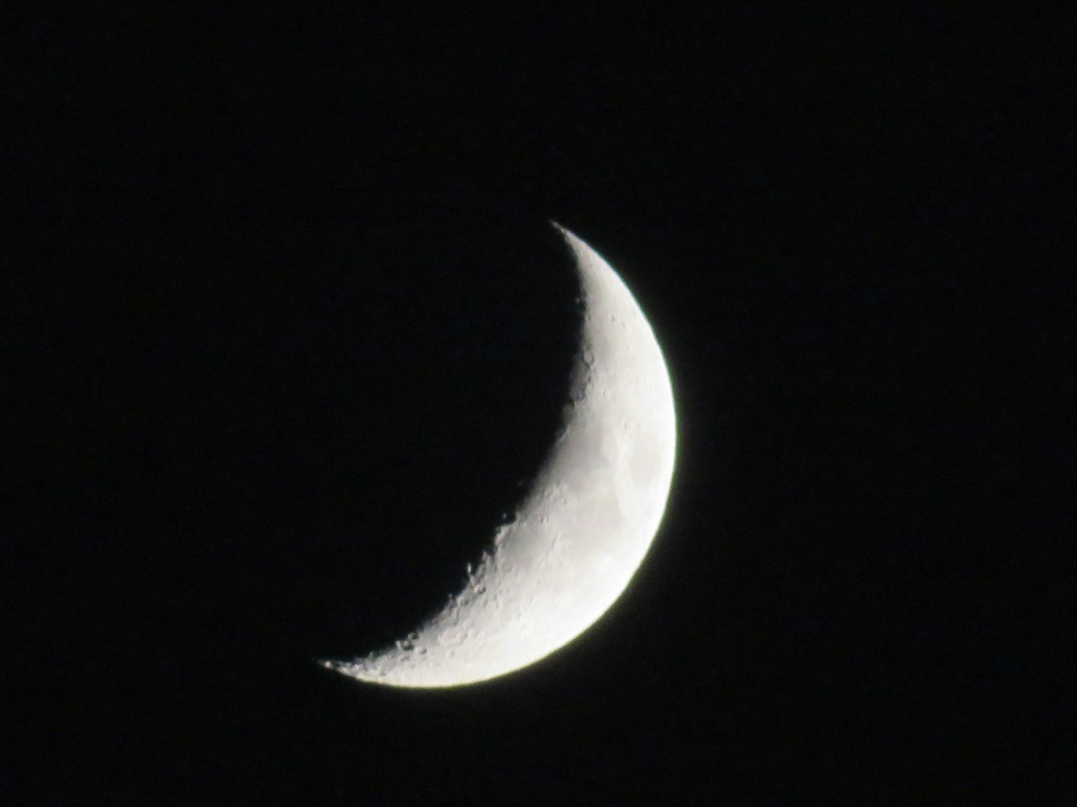 夜空中細長的彎月顯示出隕石坑和陰影