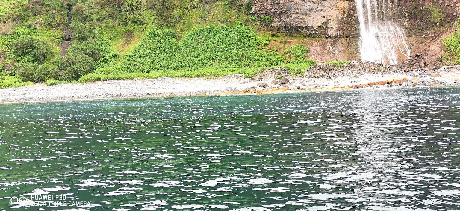 Pemandangan laut tenang dengan bukit hijau dan air terjun