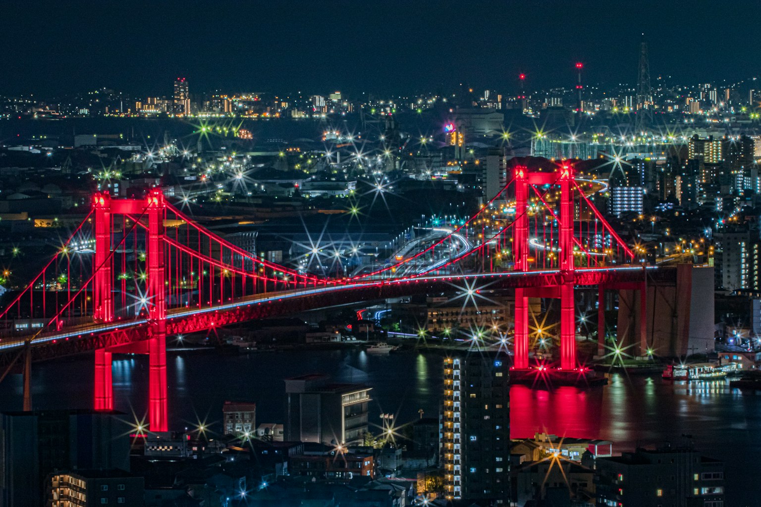 Rainbow Bridge illuminated in red against a night city skyline