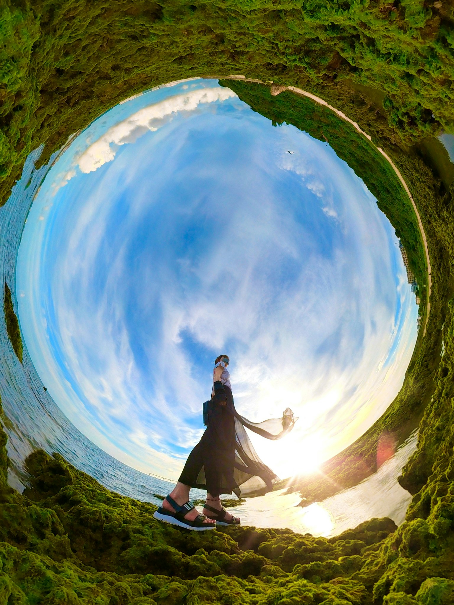Fisheye-Foto einer Frau, die an der Küste mit blauem Himmel und Sonnenlicht posiert