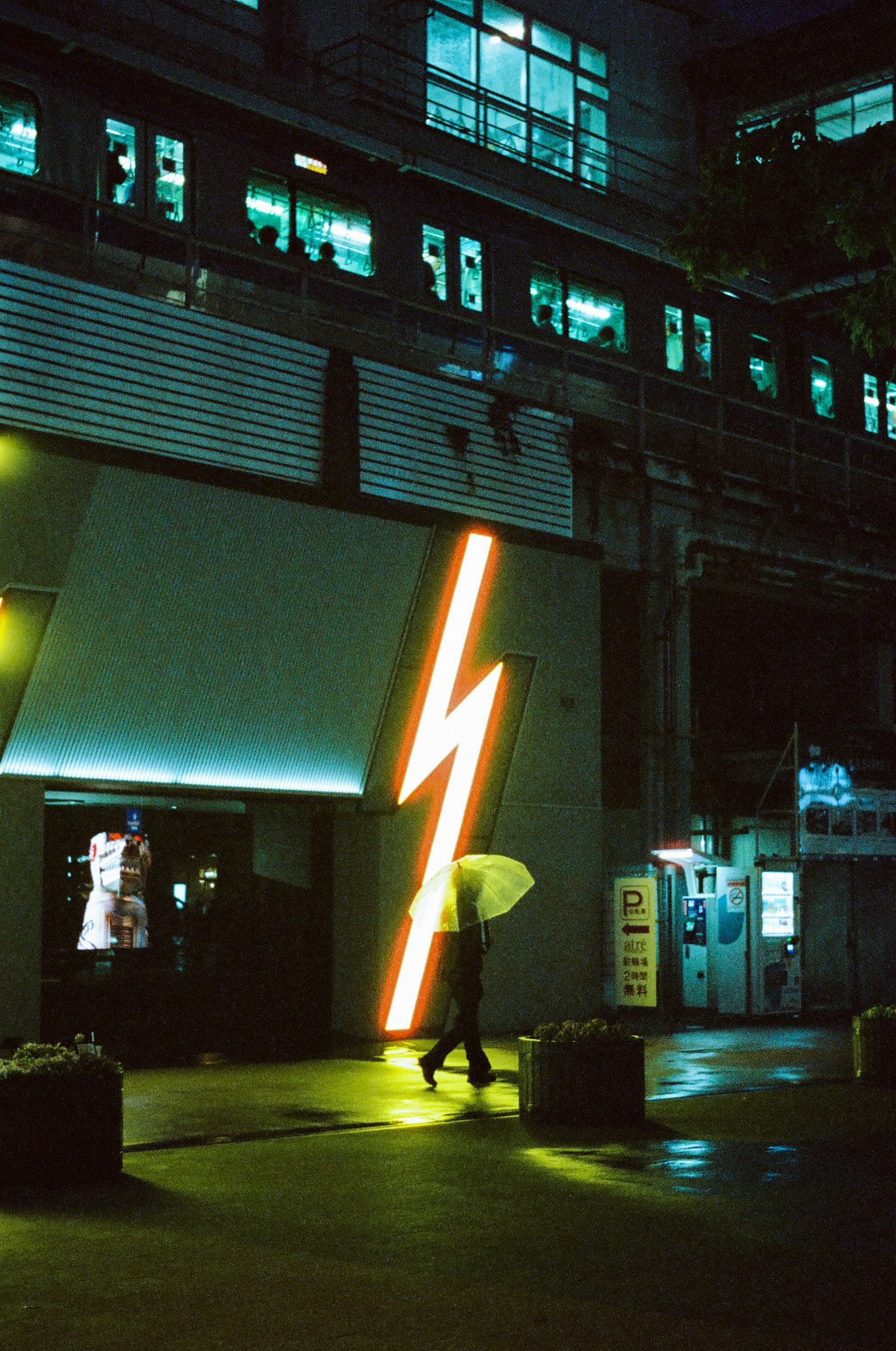 A person with an umbrella walking under a lightning neon sign at night
