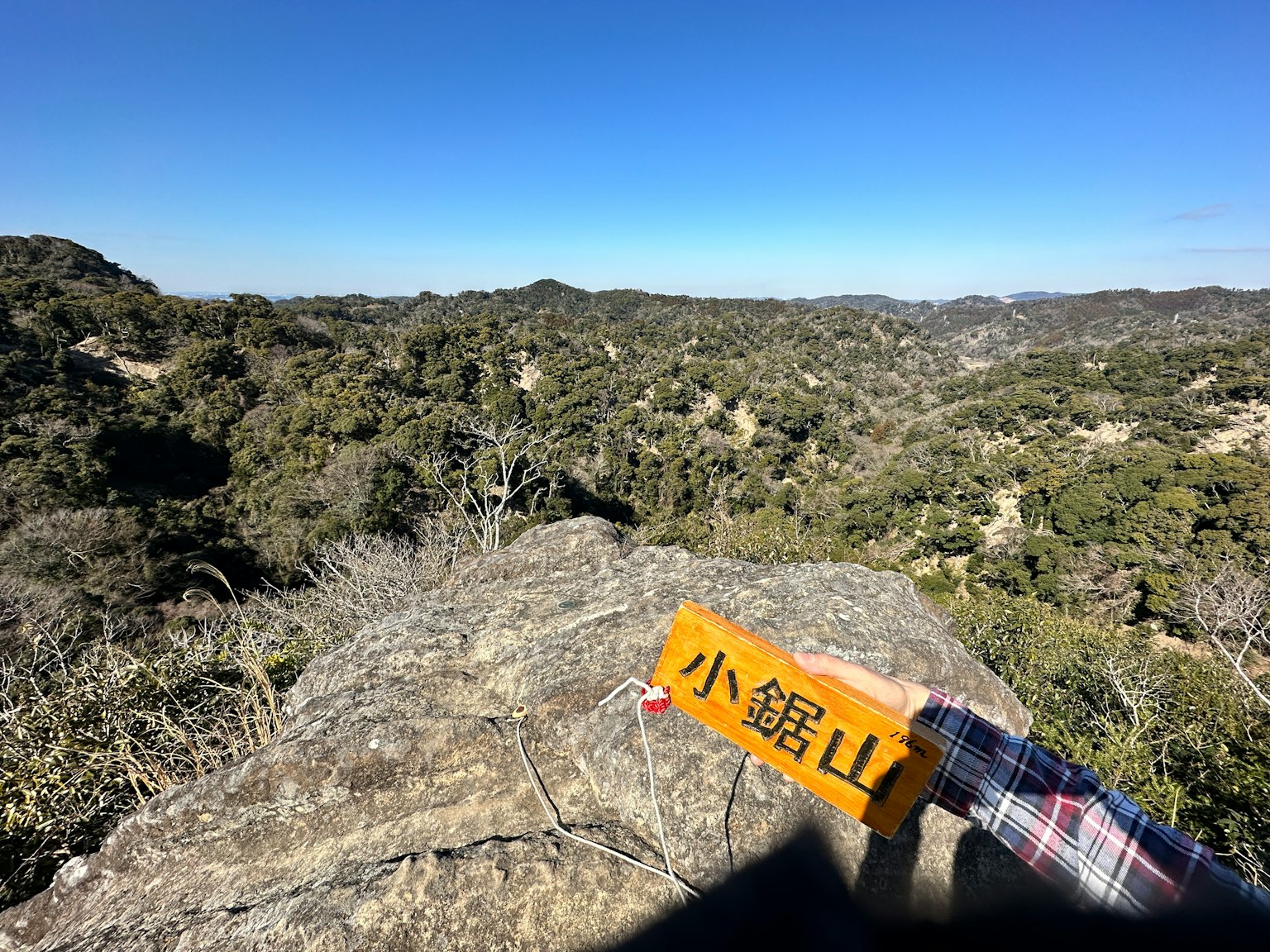 View from a rocky outcrop with a sign for Kobayashi Mountain surrounded by lush green hills and clear blue sky