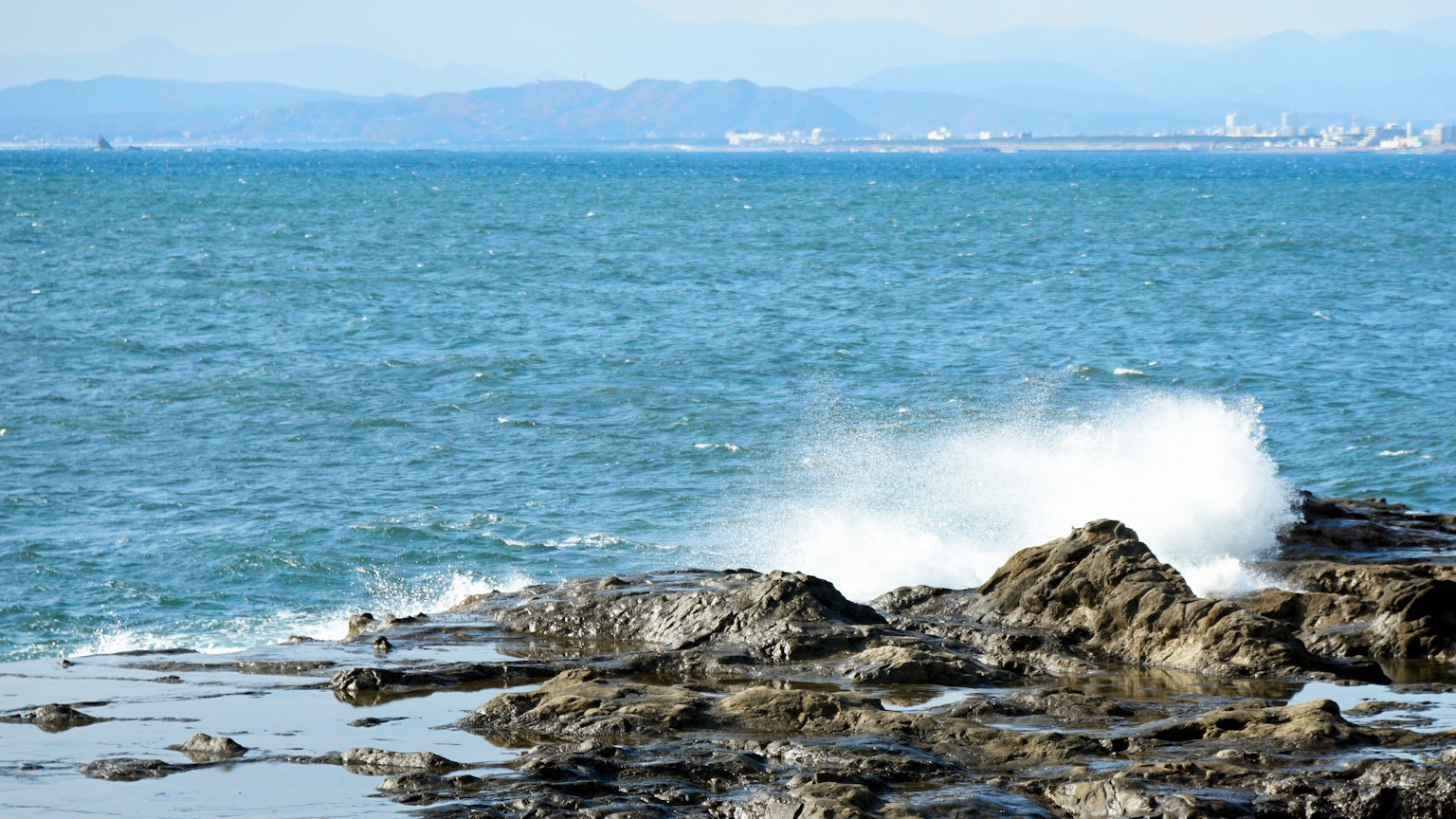 Pemandangan pantai ombak menghantam batu laut biru dan gunung di kejauhan