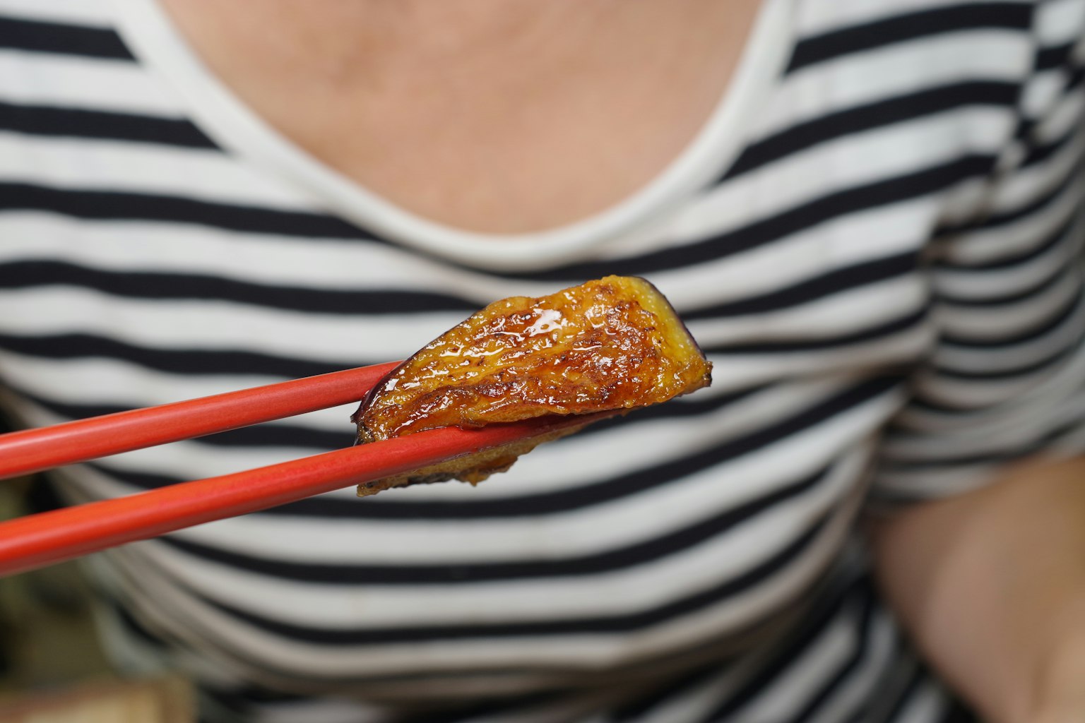 A person wearing a striped shirt holding food with red chopsticks