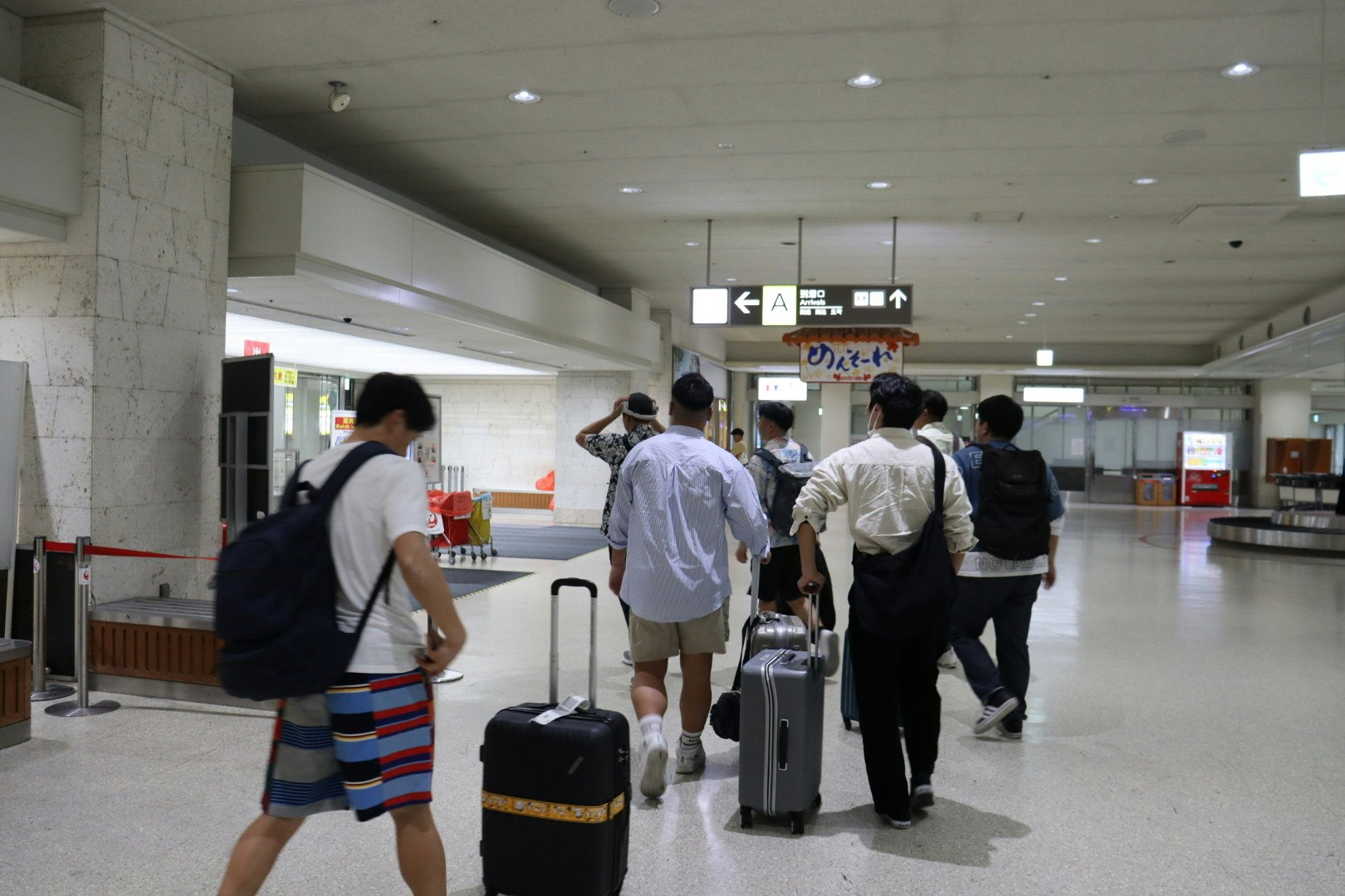 空港の広い待合ロビーでスーツケースを持つ旅行者たち