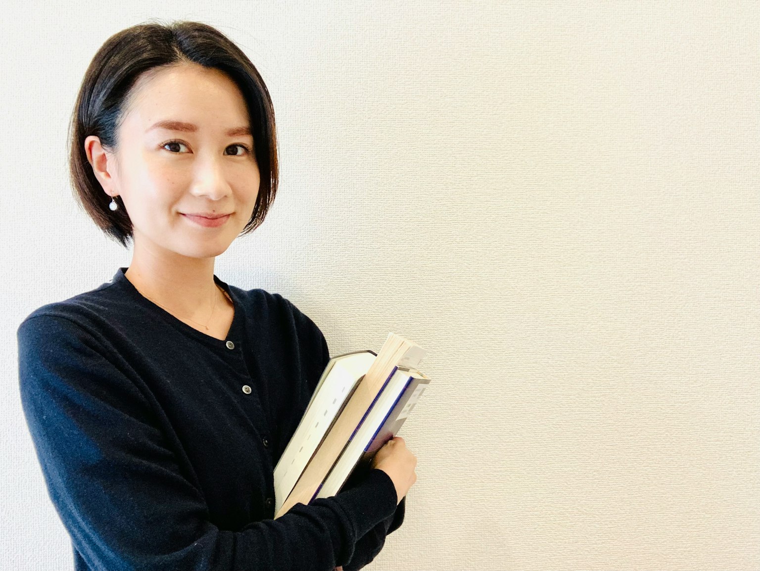 一位微笑的女性手握書本，背景簡單