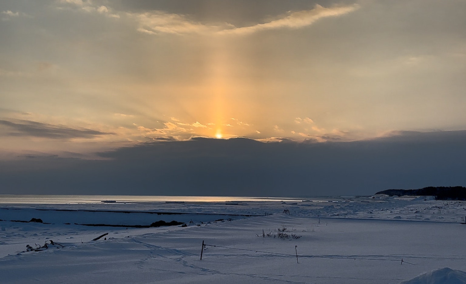 Tramonto che illumina un paesaggio innevato con raggi di luce che attraversano le nuvole