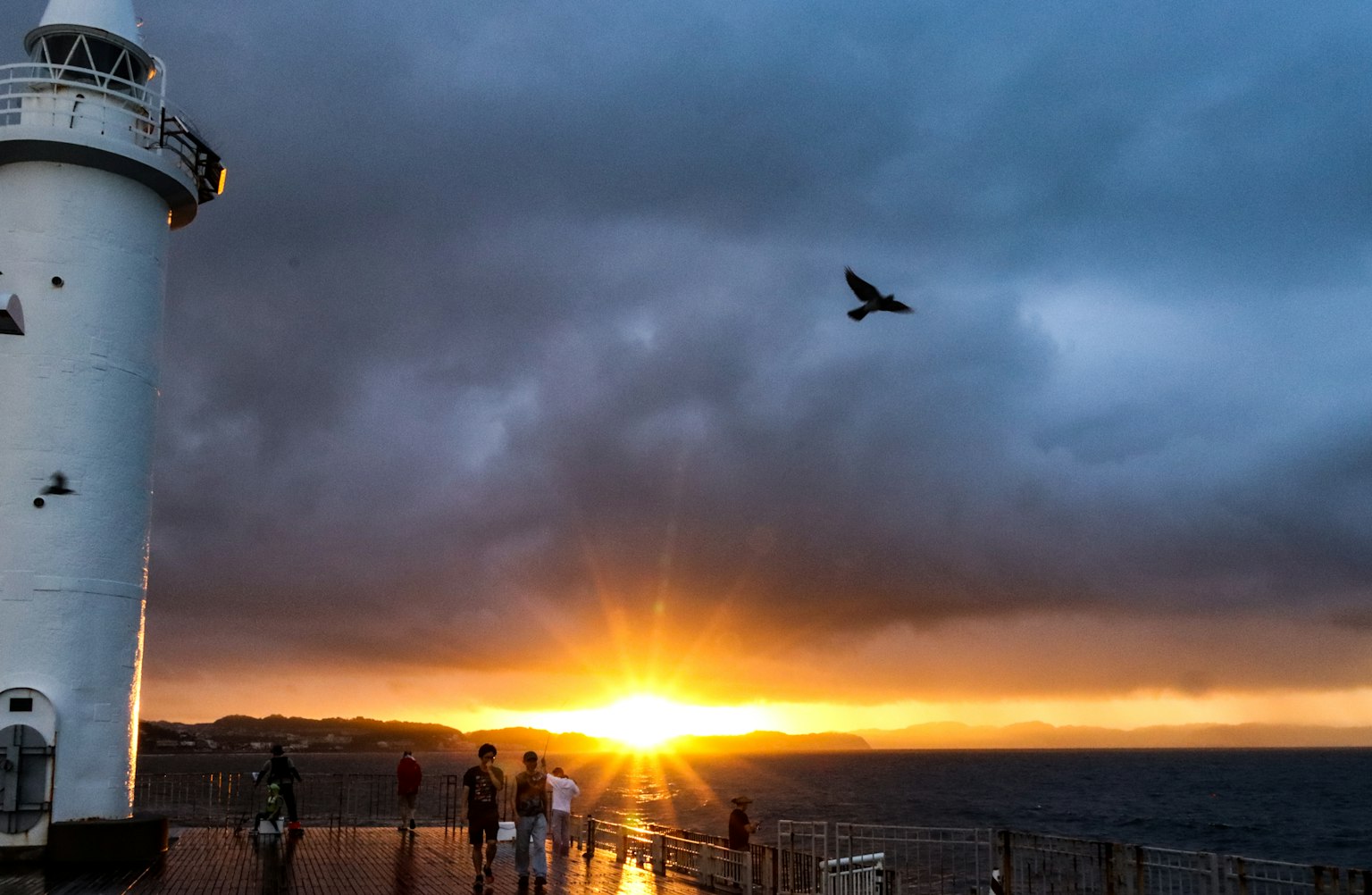 Ein Leuchtturm mit Personen silhouettiert gegen einen Sonnenuntergang über dem Ozean