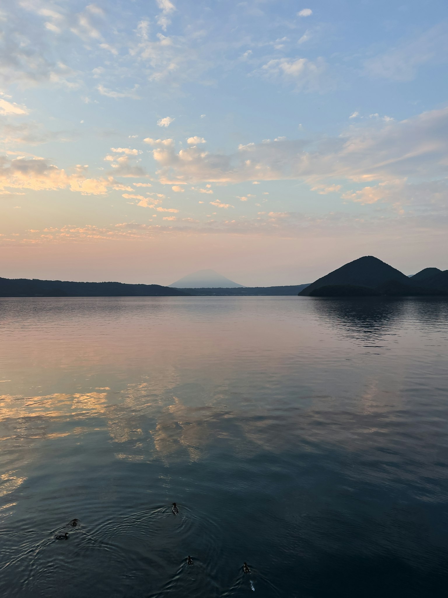 Danau tenang yang memantulkan langit senja dan siluet gunung
