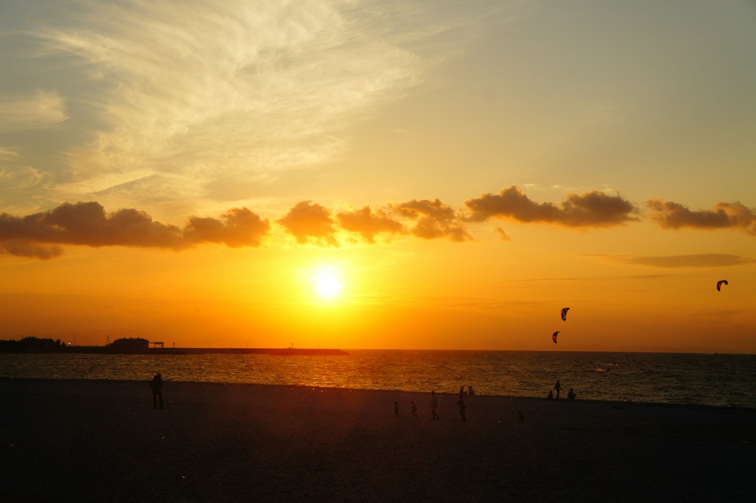 พระอาทิตย์ตกที่สวยงามเหนือมหาสมุทรพร้อมกับผู้คนที่สนุกกับการเล่นคิตเซิร์ฟ