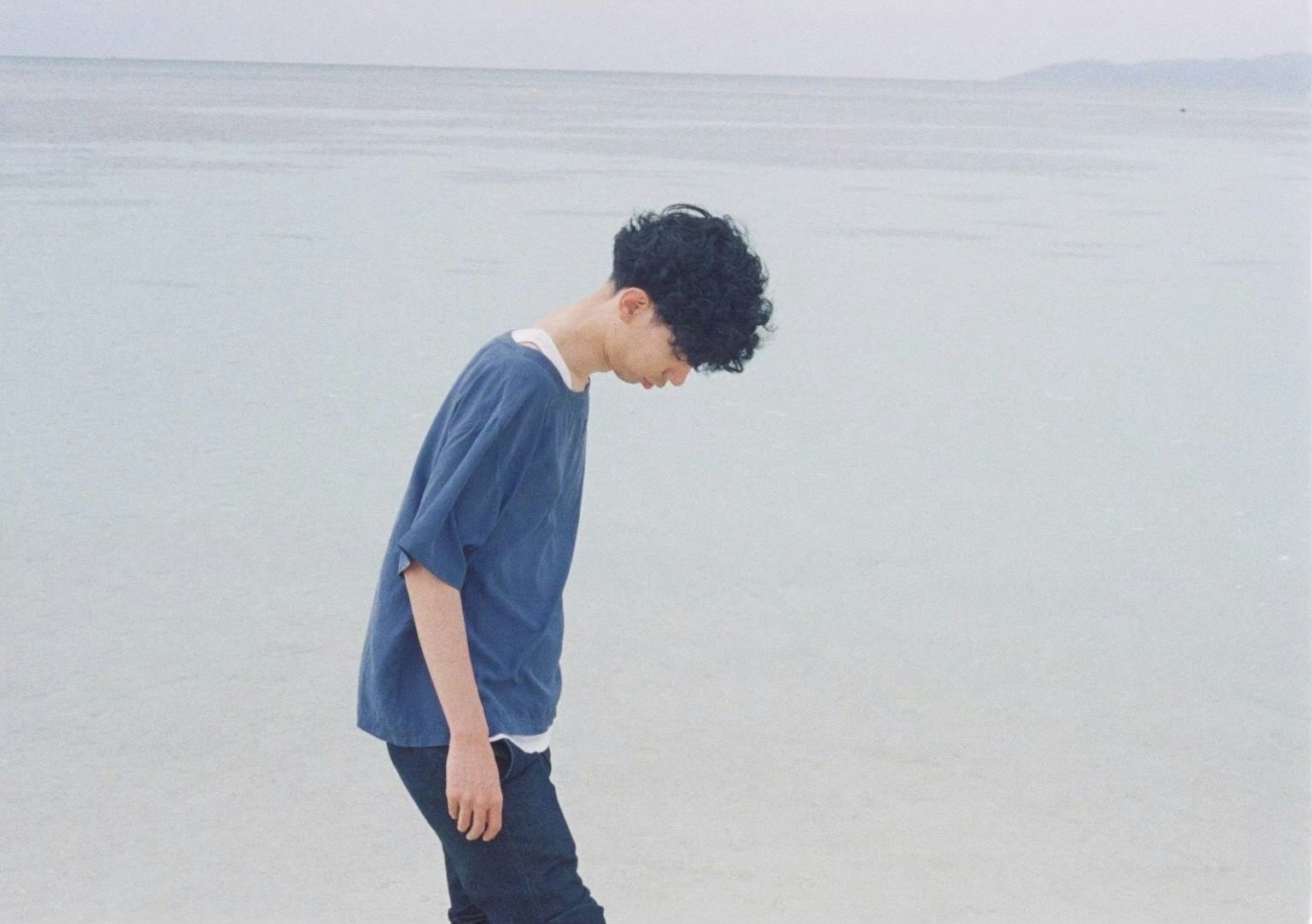 해변에서 아래를 바라보는 파란 셔츠를 입은 남자