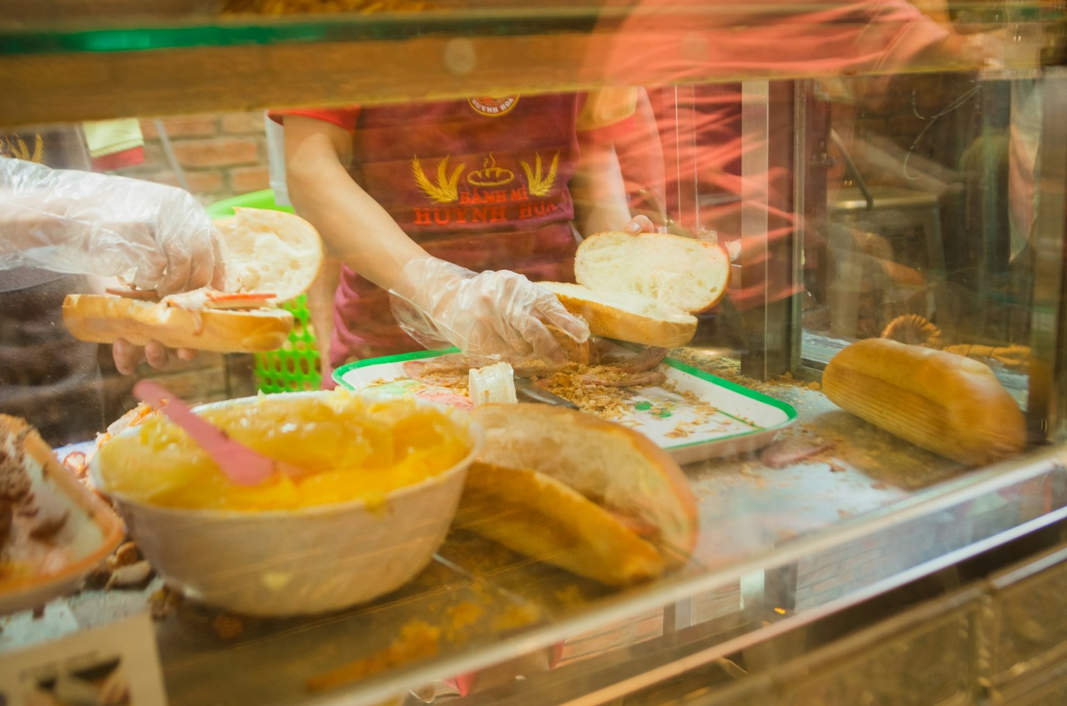 Một quầy thức ăn đang chuẩn bị bánh mì với một bàn tay đeo găng tay cầm bánh