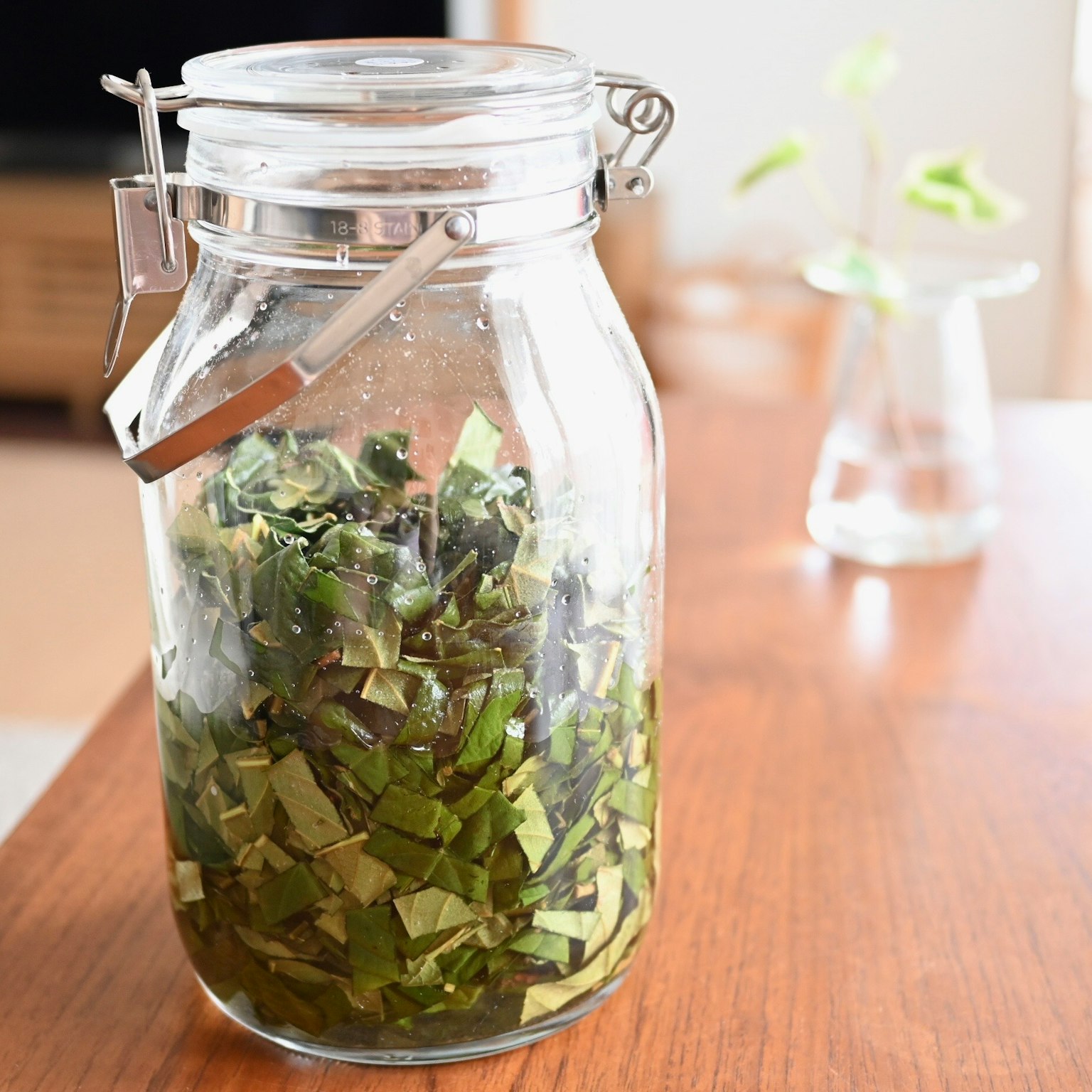 Bocal en verre rempli d'herbes vertes hachées sur une table en bois avec un petit vase en arrière-plan