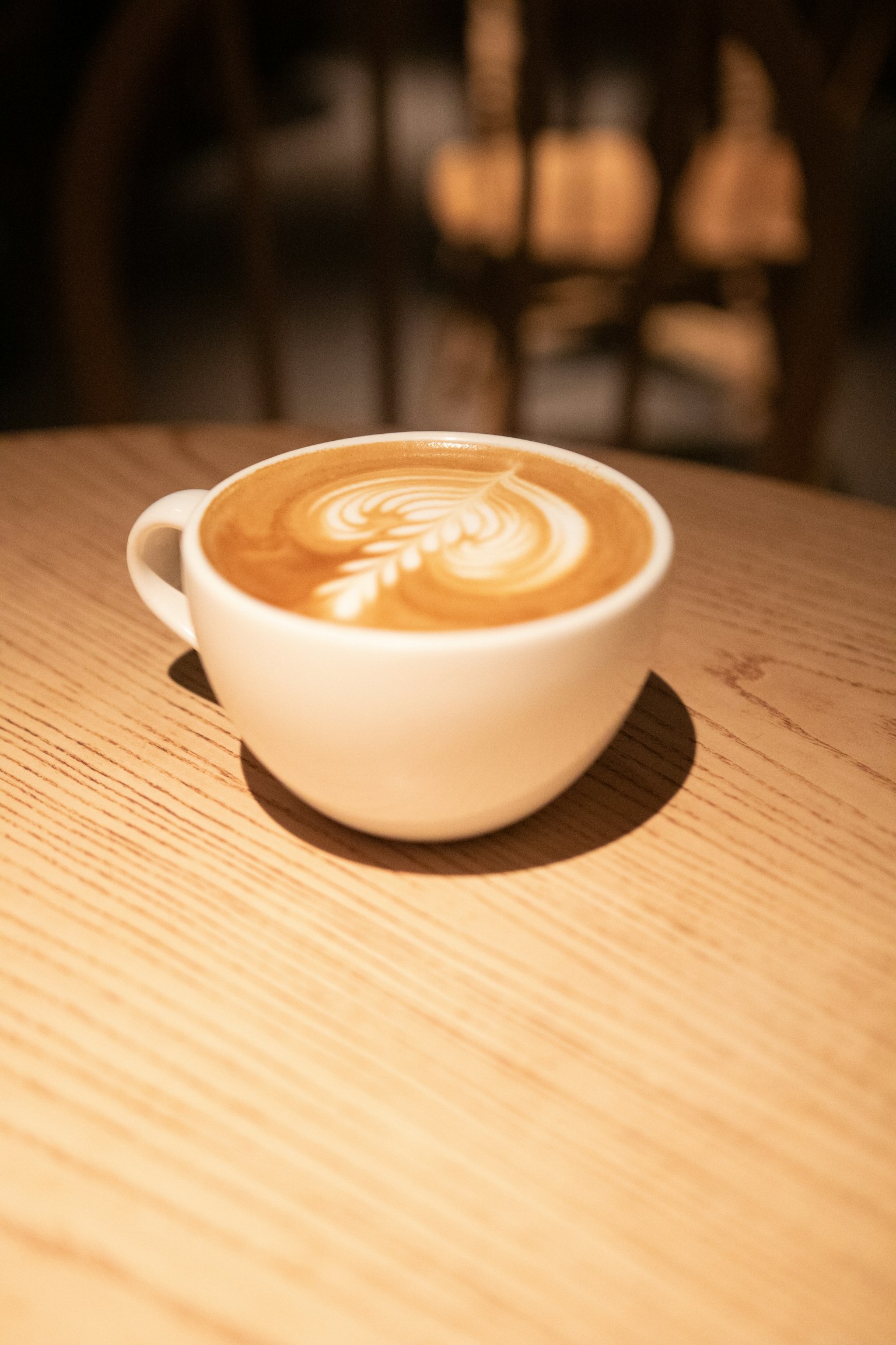 กาแฟลาเต้อาร์ตในถ้วยสีขาววางอยู่บนโต๊ะไม้