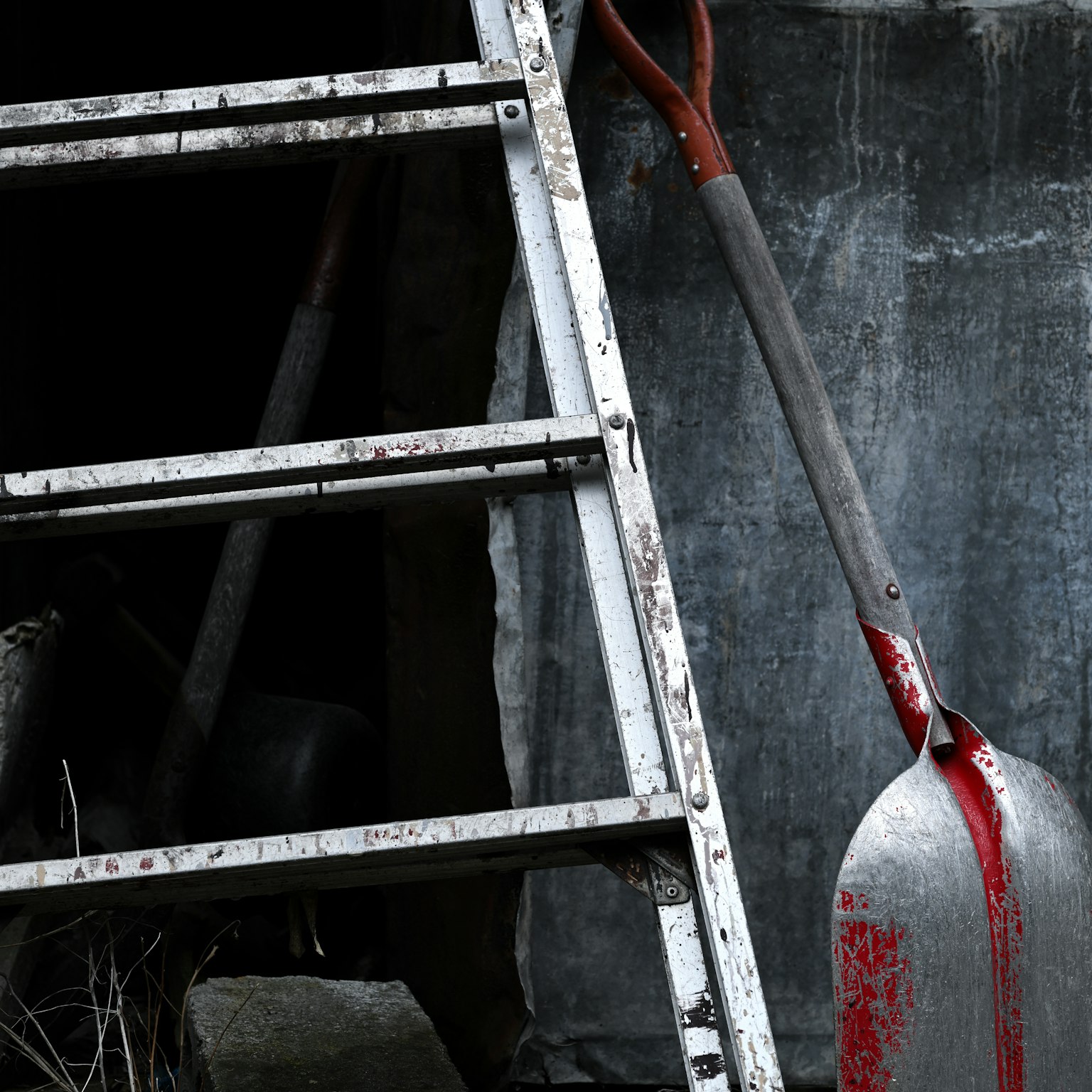 An old white ladder leaning against a dark background with a red shovel resting nearby